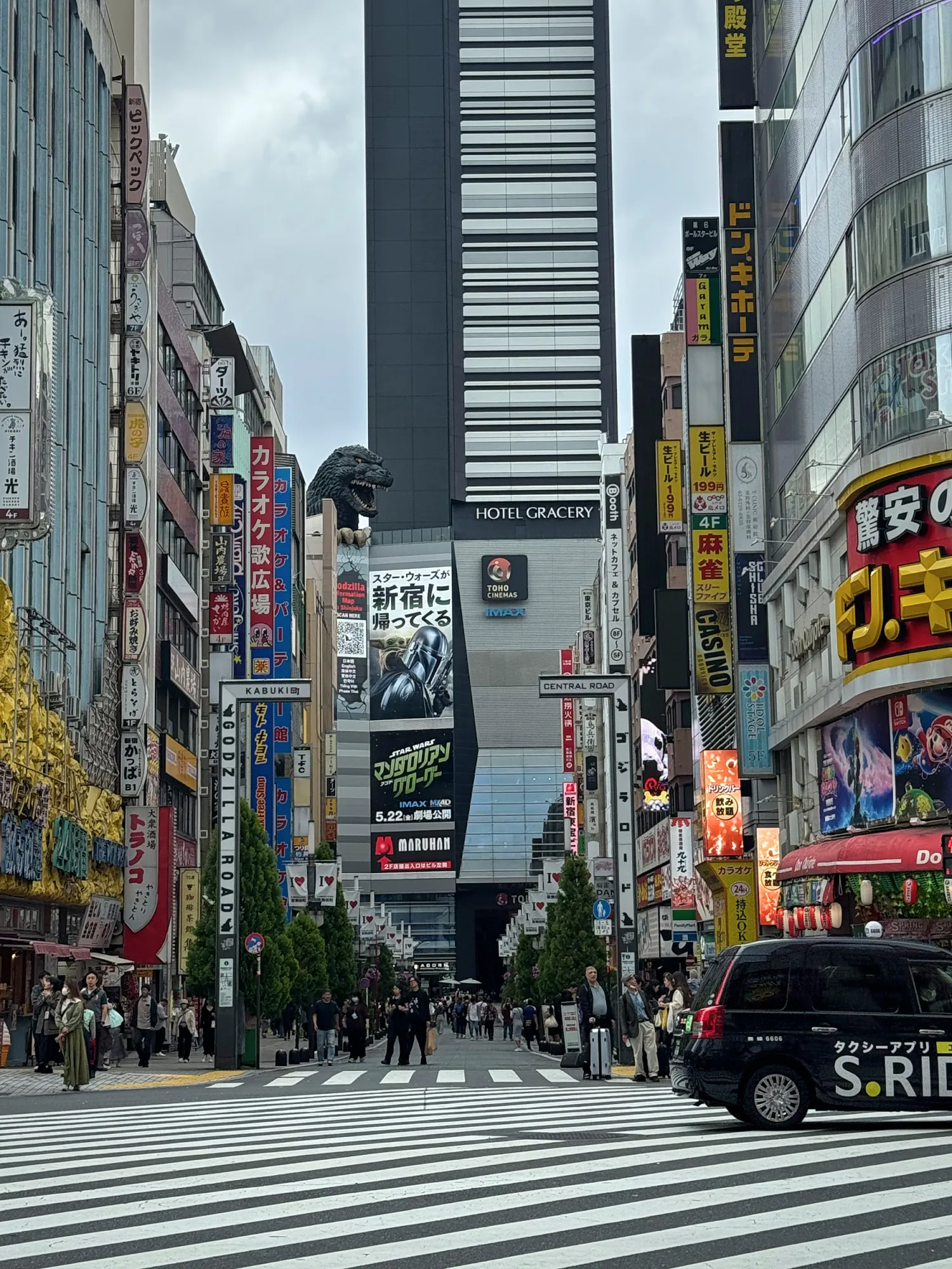 A busy Shinjuku street leading toward Hotel Gracery Shinjuku, with the Godzilla head on top of the building, Tokyo.