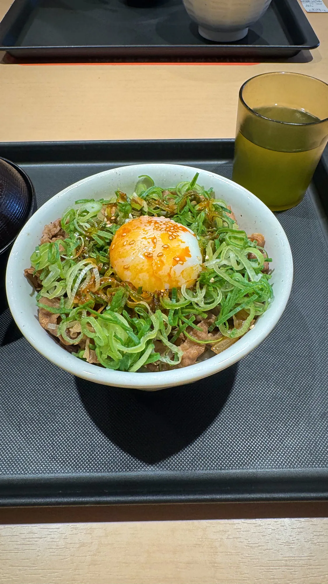 A bowl of gyudon beef over rice topped with green onions and a raw egg yolk on a tray at Matsuya in Tokyo.