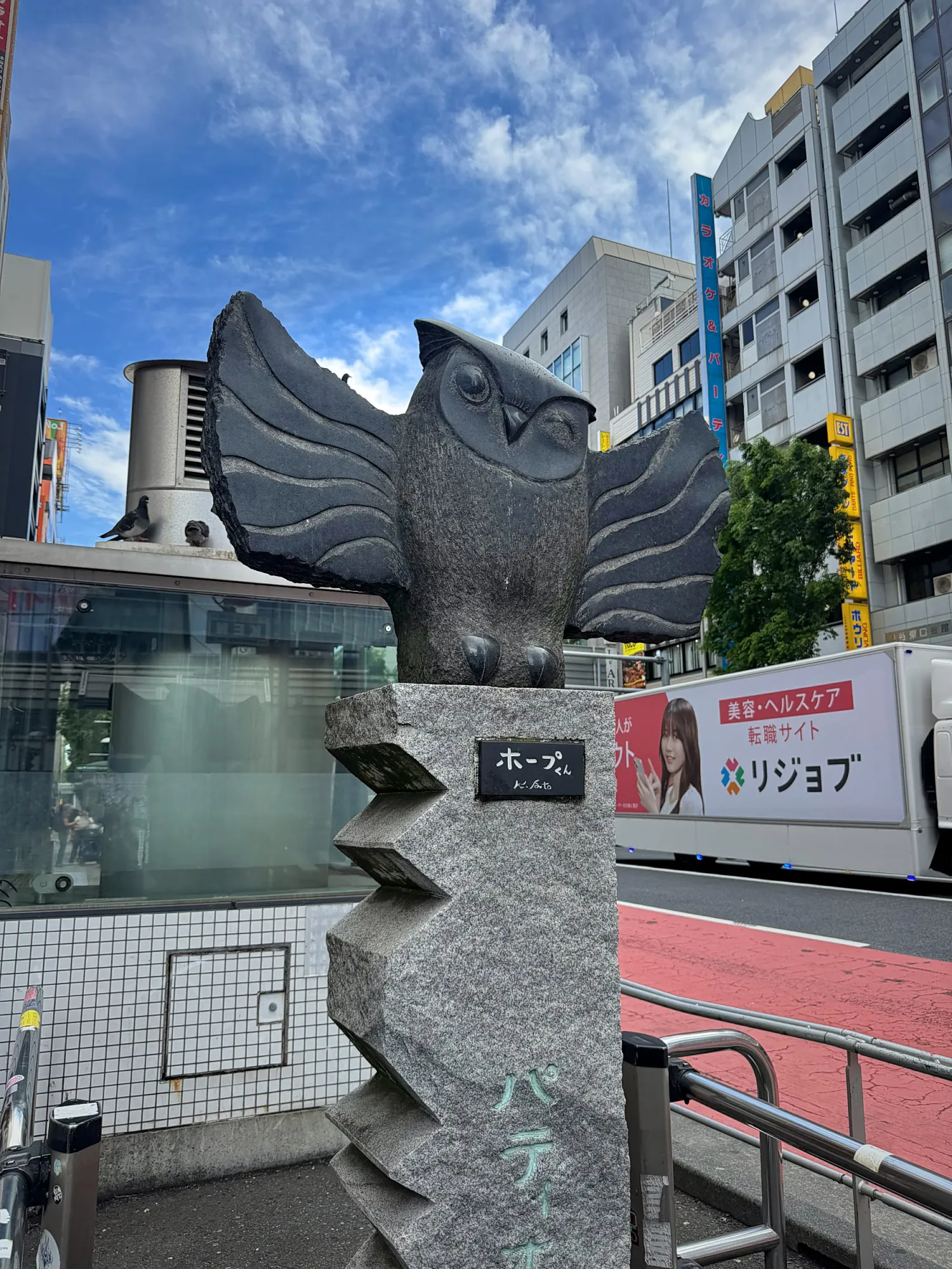 A stone owl statue on a pillar near Ikebukuro Station in Tokyo, under a blue sky.