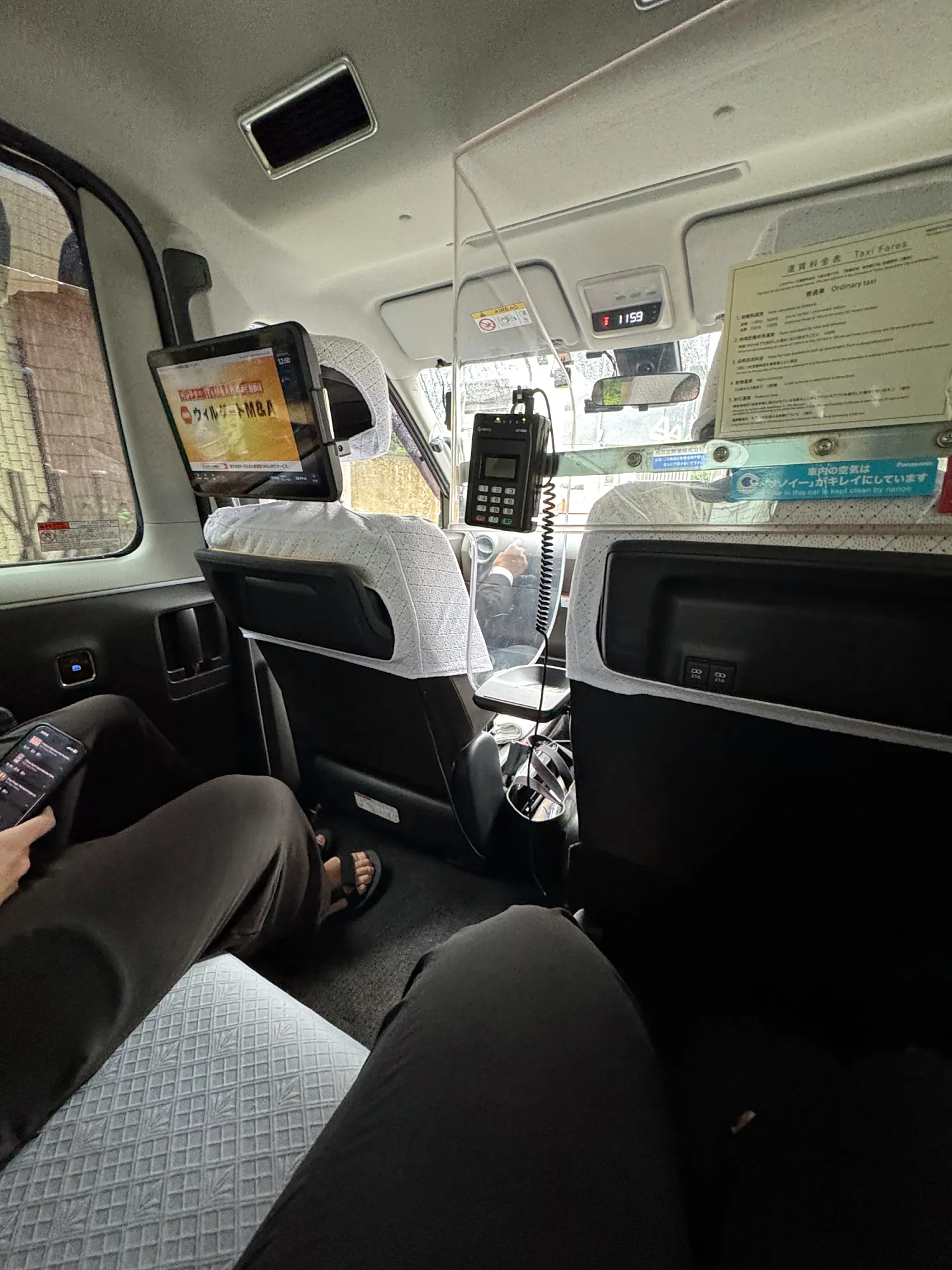 The back seat of a Tokyo taxi, with lace seat covers and a screen on the back of the front seat.