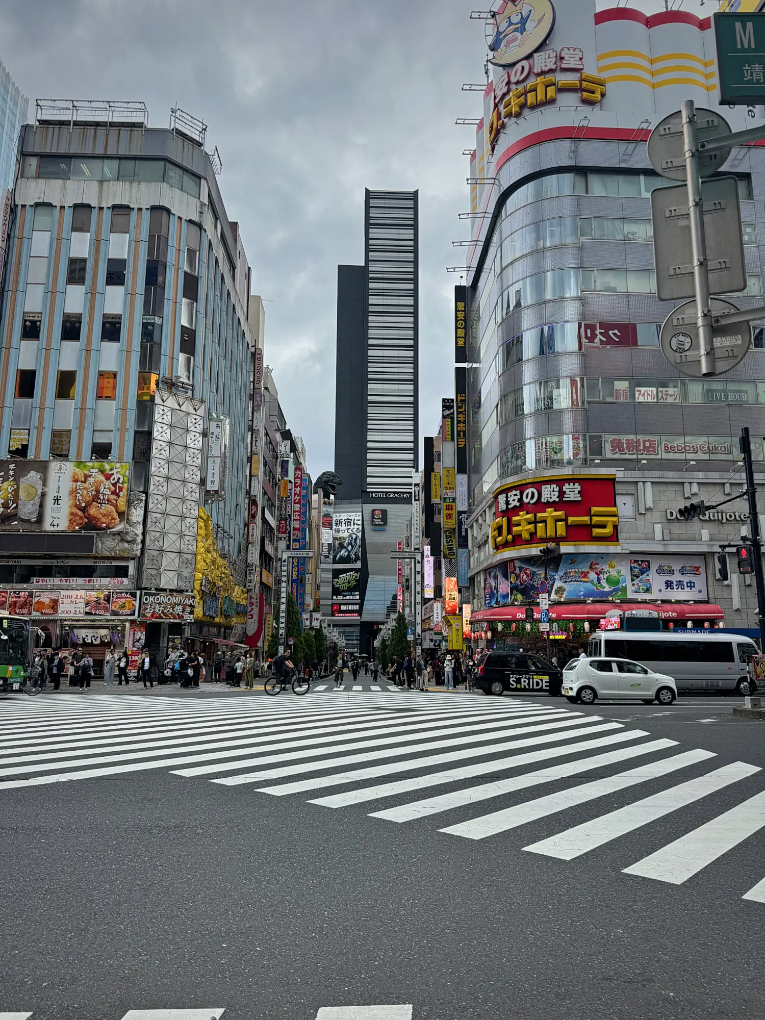 A wide crosswalk at the entrance to Kabukicho in Shinjuku, Tokyo, with tall buildings and signs on both sides.