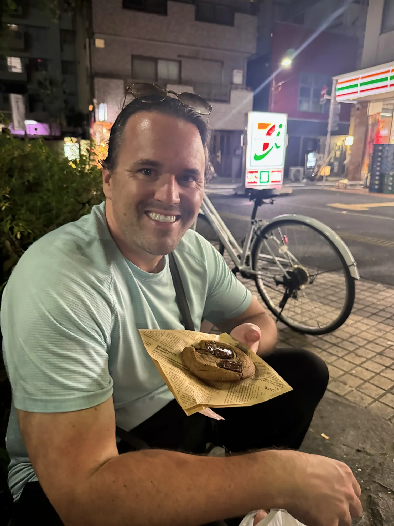 Cream smiling with a 7-Eleven chocolate cookie outside a 7-Eleven at night in Tokyo.