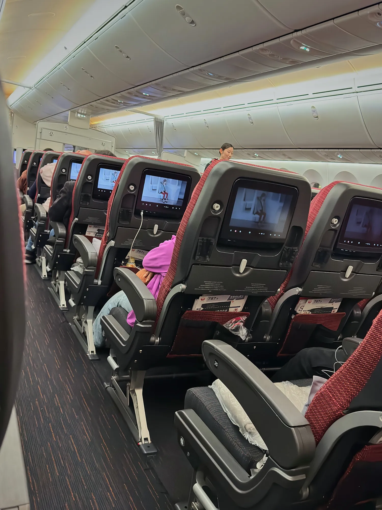 Rows of airplane seats with seatback screens and passengers settled in on a long-haul flight to Tokyo.