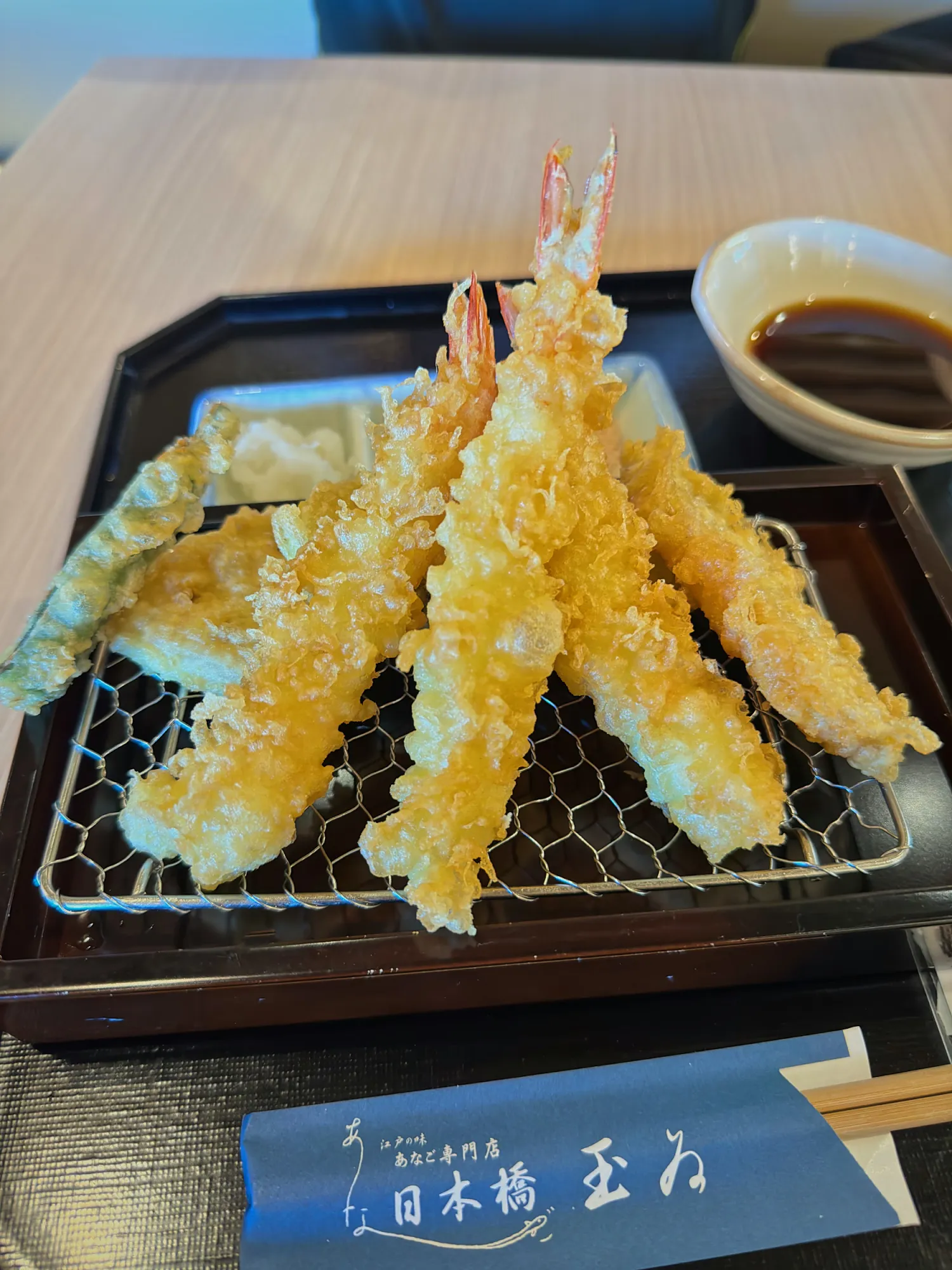 Golden shrimp and vegetable tempura on a wire rack with dipping sauce at Tempura Nihonbashi Tamai, Narita Airport.