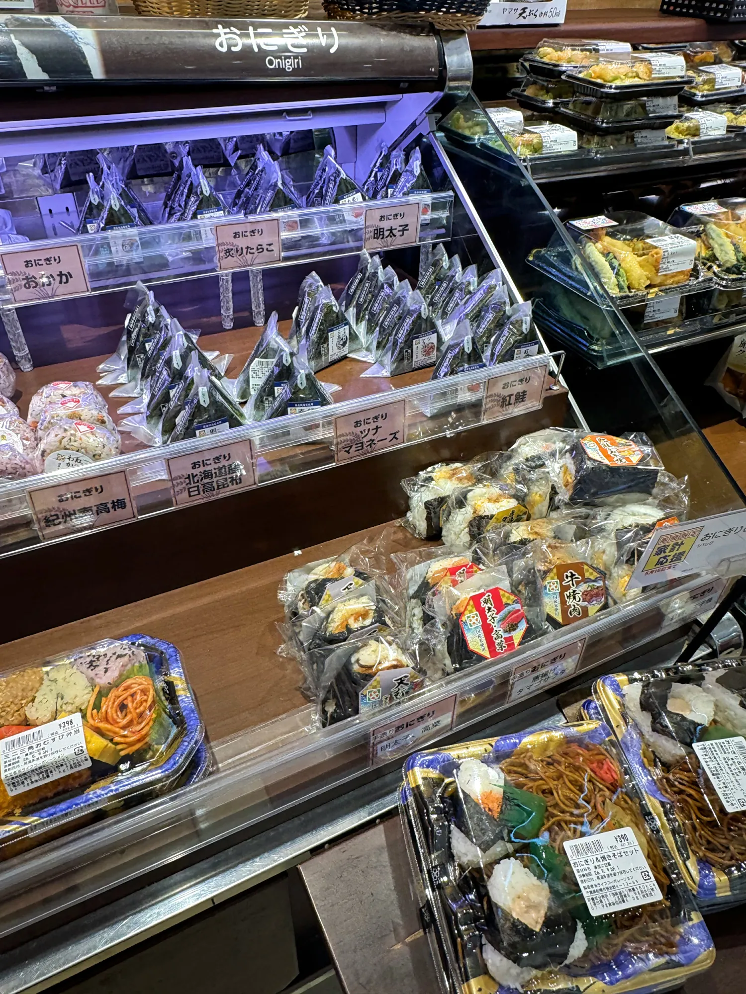 A convenience store shelf in Tokyo stacked with wrapped onigiri rice balls and bento boxes.
