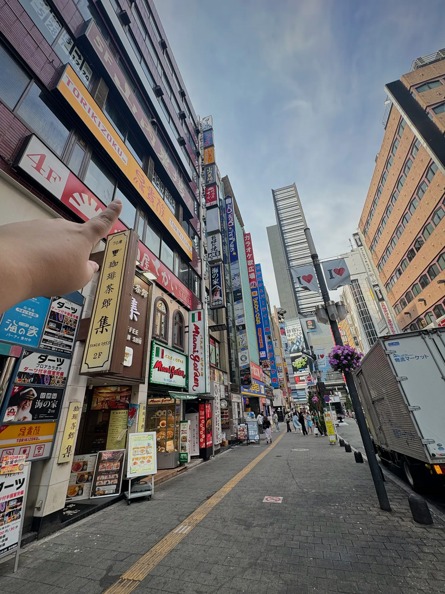 A hand pointing up at stacked restaurant signs running up the side of buildings on a Shinjuku street in Tokyo.
