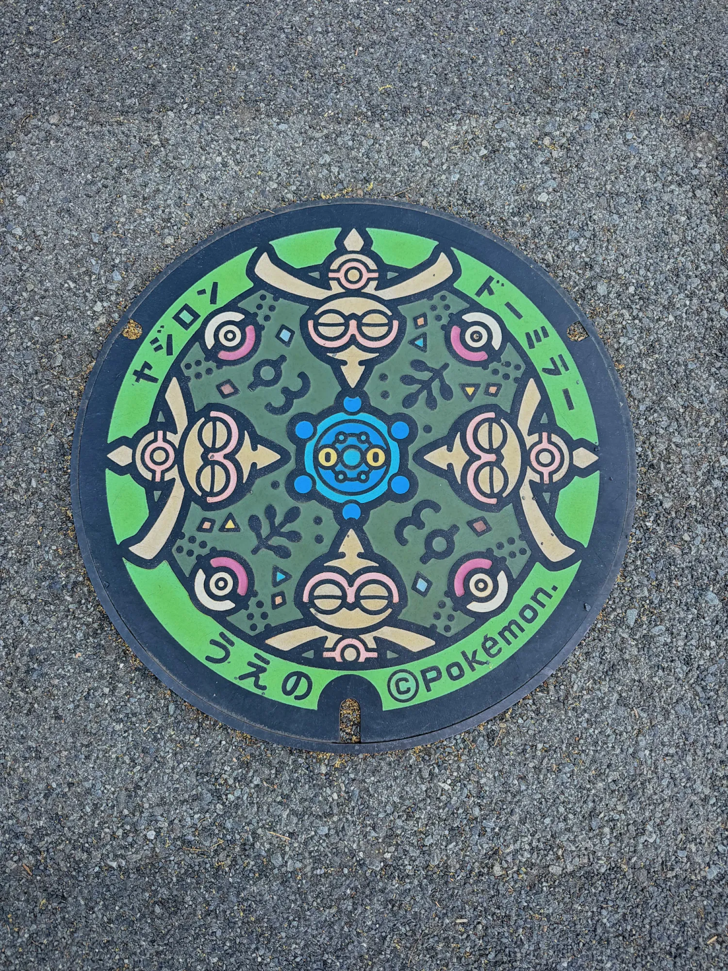 A colorful Pokémon manhole cover with Baltoy and Bronzor and the word Ueno in Japanese, in Ueno Park, Tokyo.