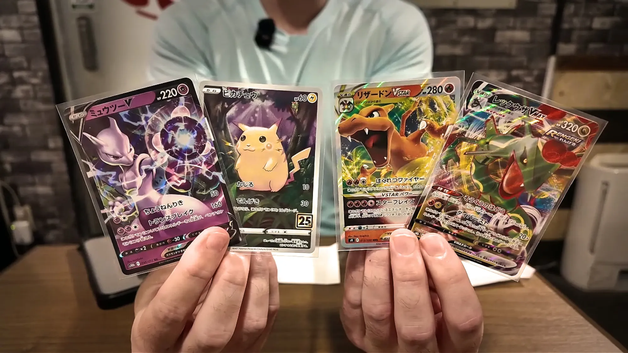 Hands holding up the four Japanese Pokémon cards we bought: Mewtwo V, Pikachu, Charizard VSTAR, and Rayquaza VMAX.