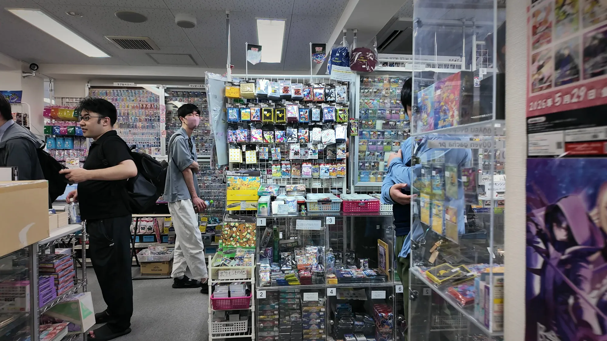 Shoppers browsing glass cases and shelves of Pokémon cards inside a busy trading card shop in Tokyo.