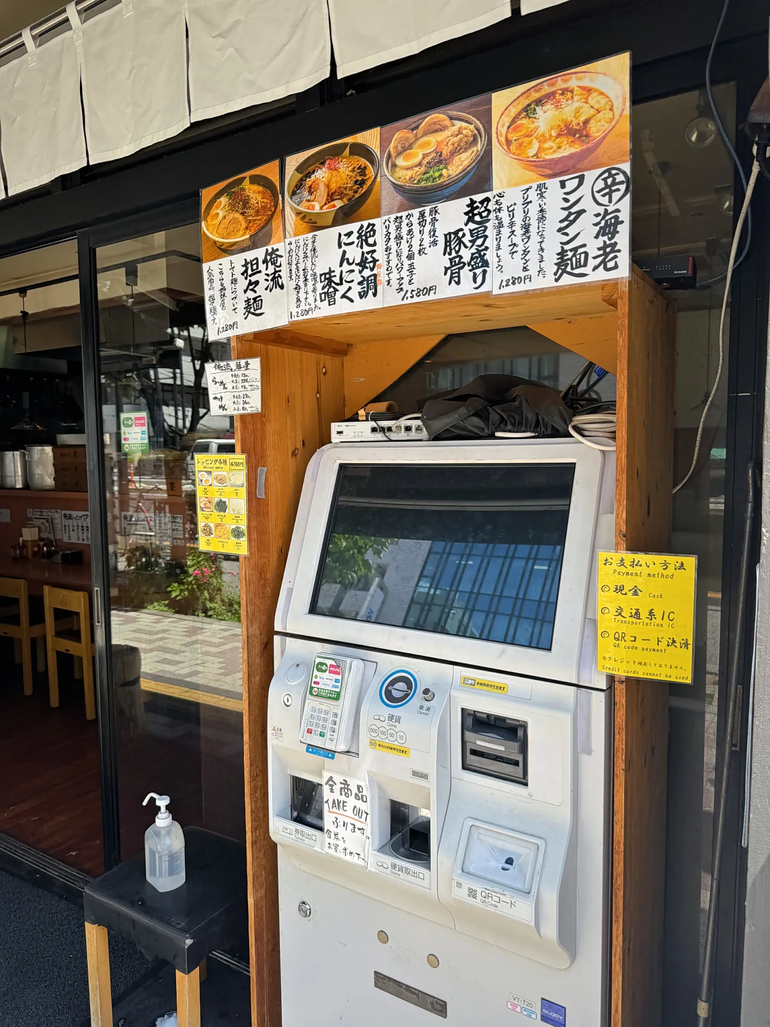 A meal ticket machine outside a Tokyo ramen shop, with a yellow sticker beside it listing cash, transit IC cards, and QR code payment.