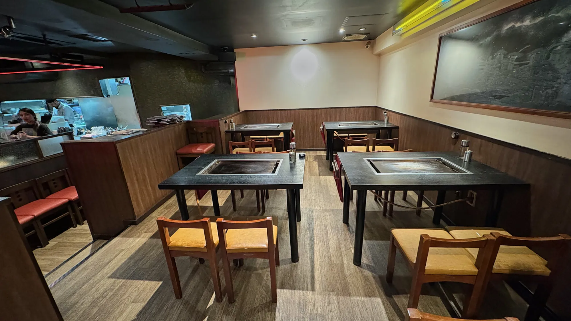 Wooden tables with built-in teppan griddles and red and yellow chairs inside Osakaya restaurant in Shinjuku, Tokyo.