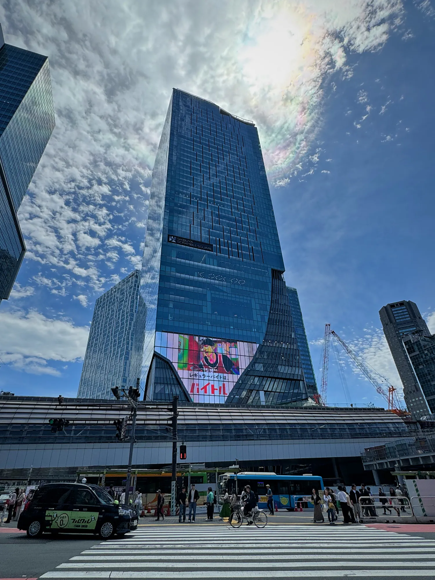 The glass Shibuya Scramble Square tower rising over Shibuya Station under a bright blue sky with big white clouds.