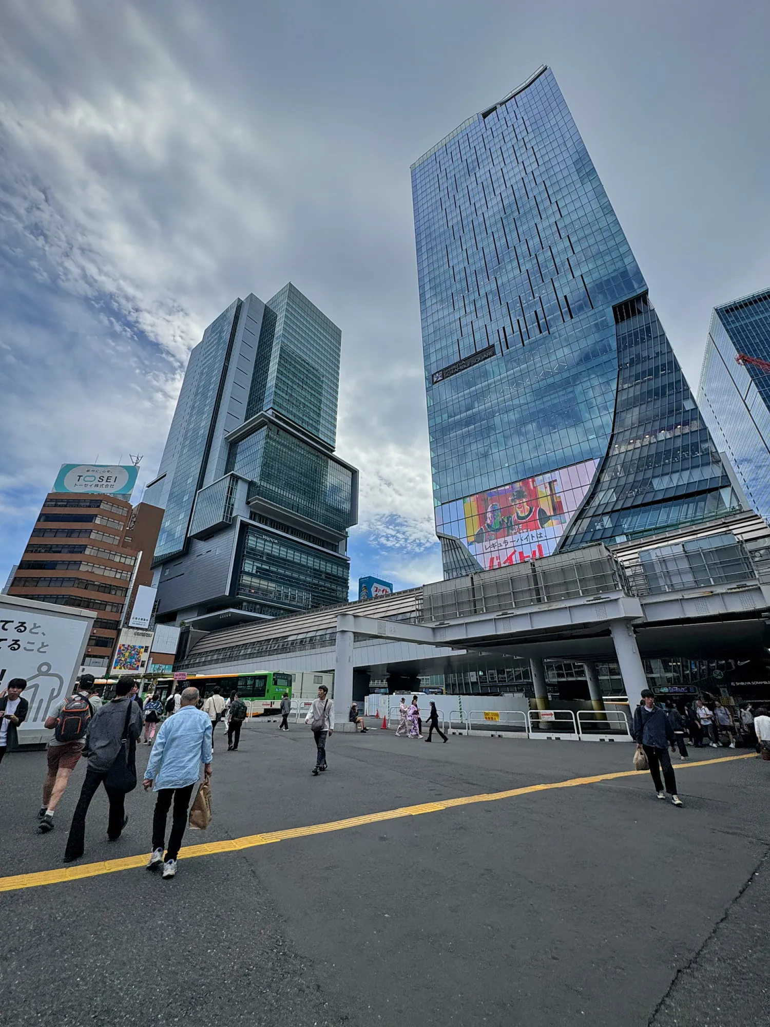 People crossing at Shibuya Crossing under glass skyscrapers including Shibuya Scramble Square, Tokyo.