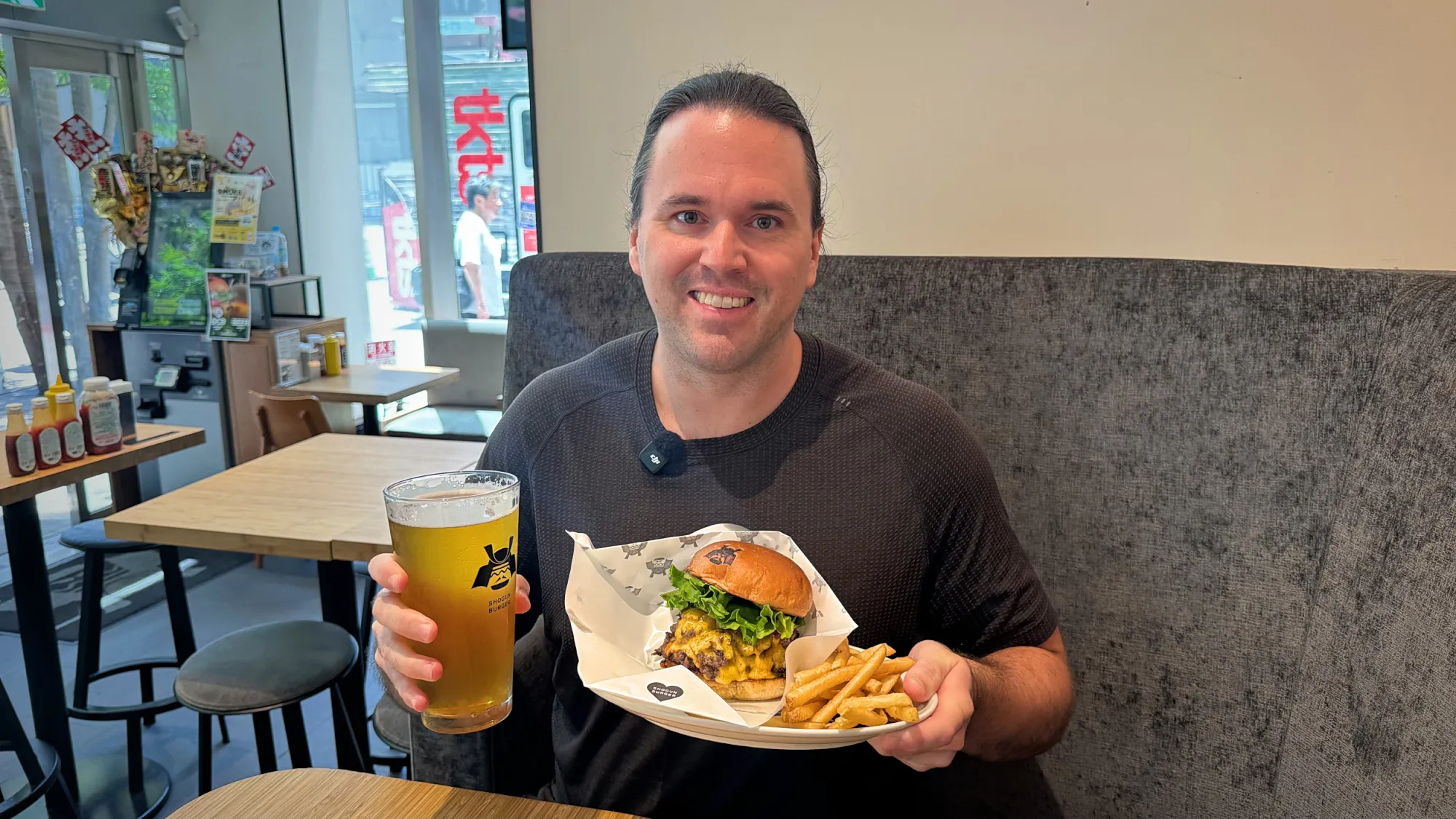 Cream holding a Shogun Burger cheeseburger and fries in one hand and a beer in the other
