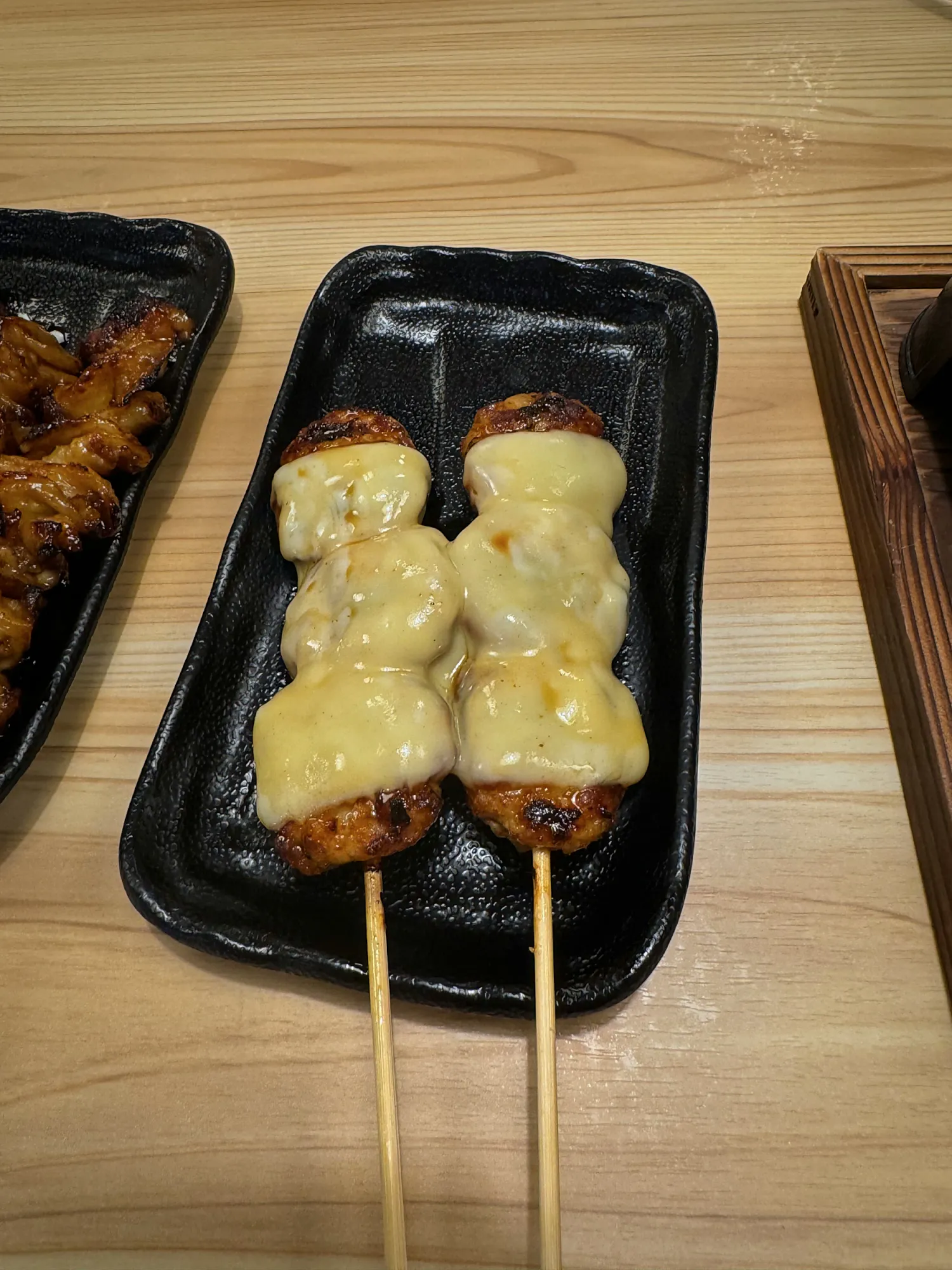 Two chicken meatball skewers topped with melted cheese on a black plate at Torikizoku, Tokyo.