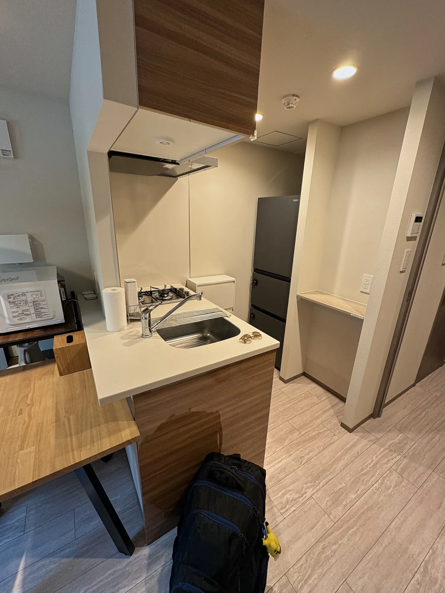 The compact kitchen in our monthly Airbnb in Tokyo, with a sink, a two-burner gas stove, wood cabinets, and a tall dark fridge.