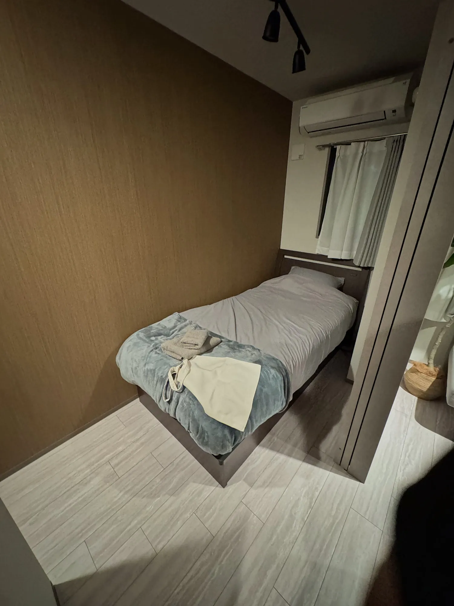 A single bed with a gray cover in the small bedroom of our monthly Airbnb in Tokyo, under a wall air conditioner.