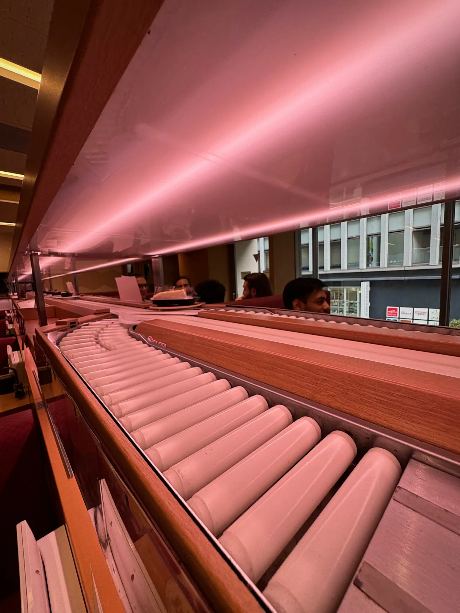 The empty express lane at Sushiro in Tokyo, a long roller track lit in pink running past the tables.