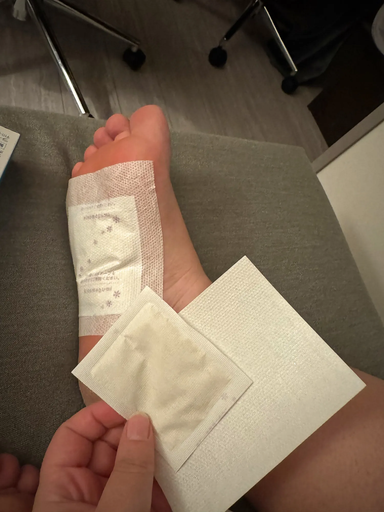 A traveler sticking a white Japanese foot patch onto the sole of their foot after a long day of walking in Tokyo.