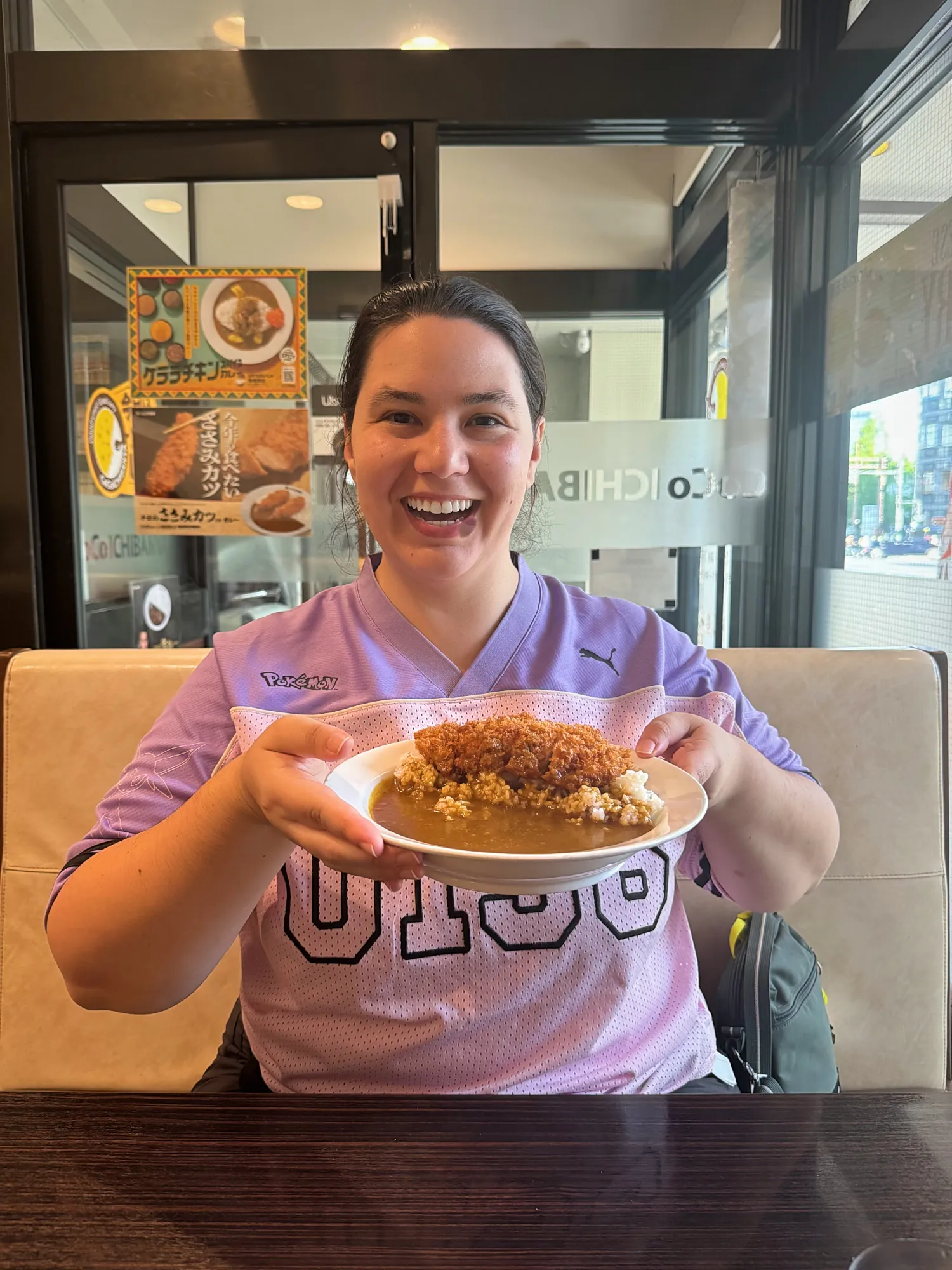 Bernie laughing in a CoCo Ichibanya booth as she holds up her katsu curry
