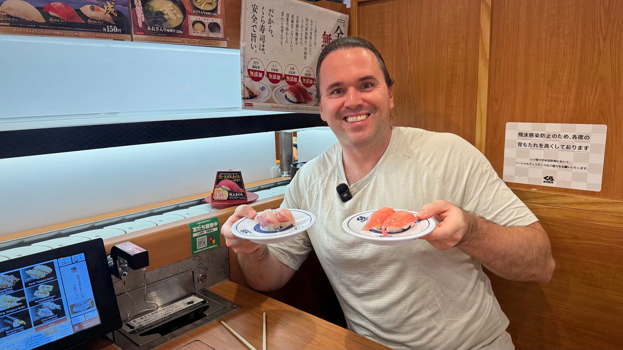 Cream holding up two plates of sushi at a Kura Sushi booth by the conveyor belt