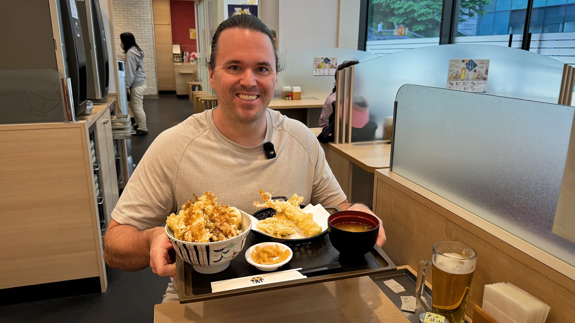 Cream smiling as he holds up a tray with a tempura bowl, miso soup, and pickles at Tenya