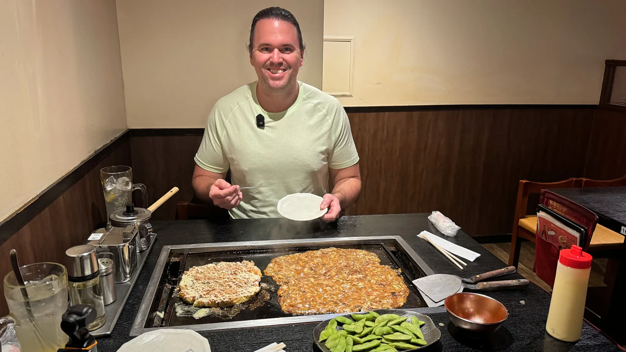 Cream smiling behind the griddle at Osakaya with okonomiyaki and monjayaki cooking in front of him
