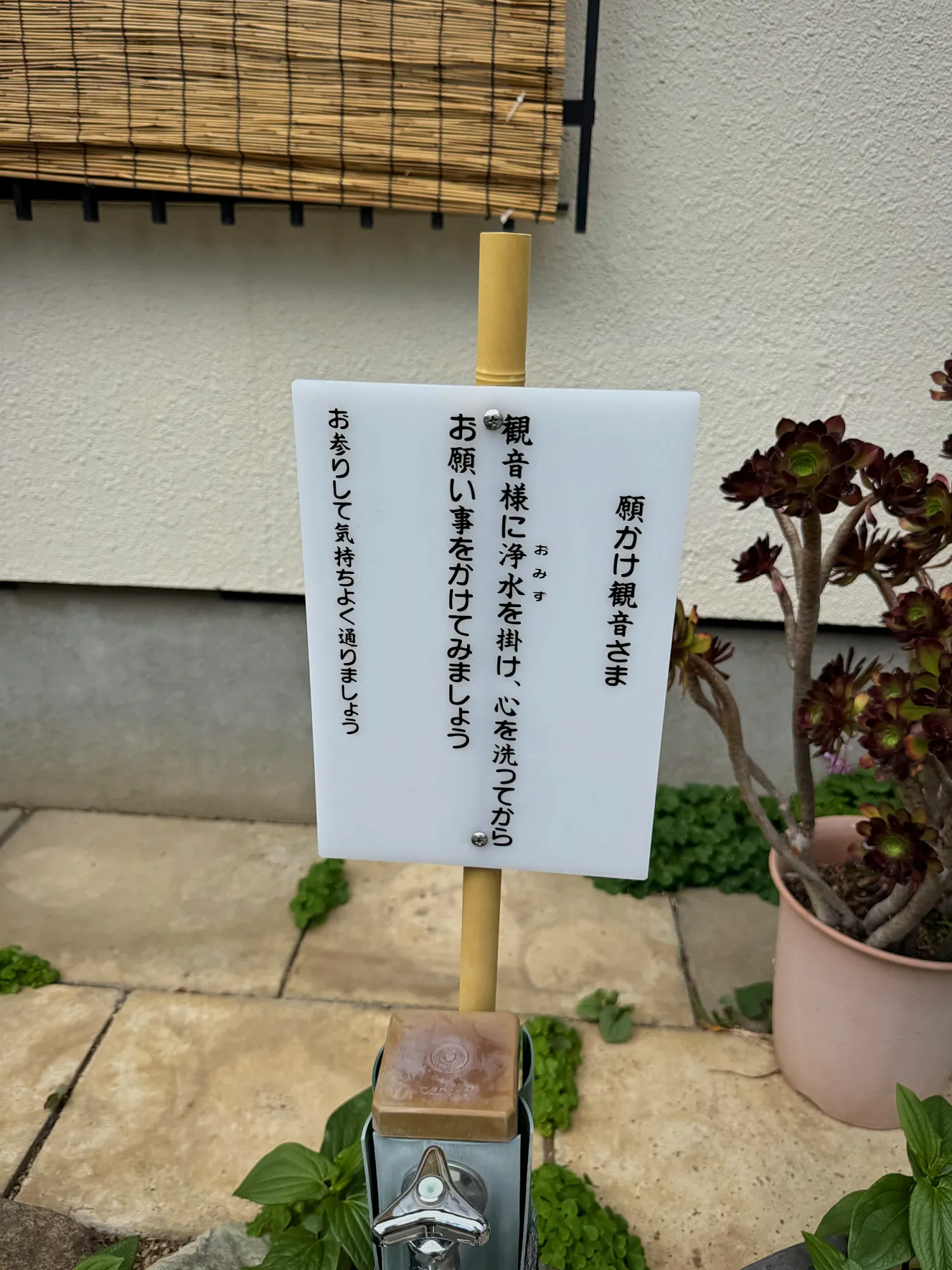 A handwritten notice in Japanese on a wooden post in a small garden in Shinjuku, Tokyo.
