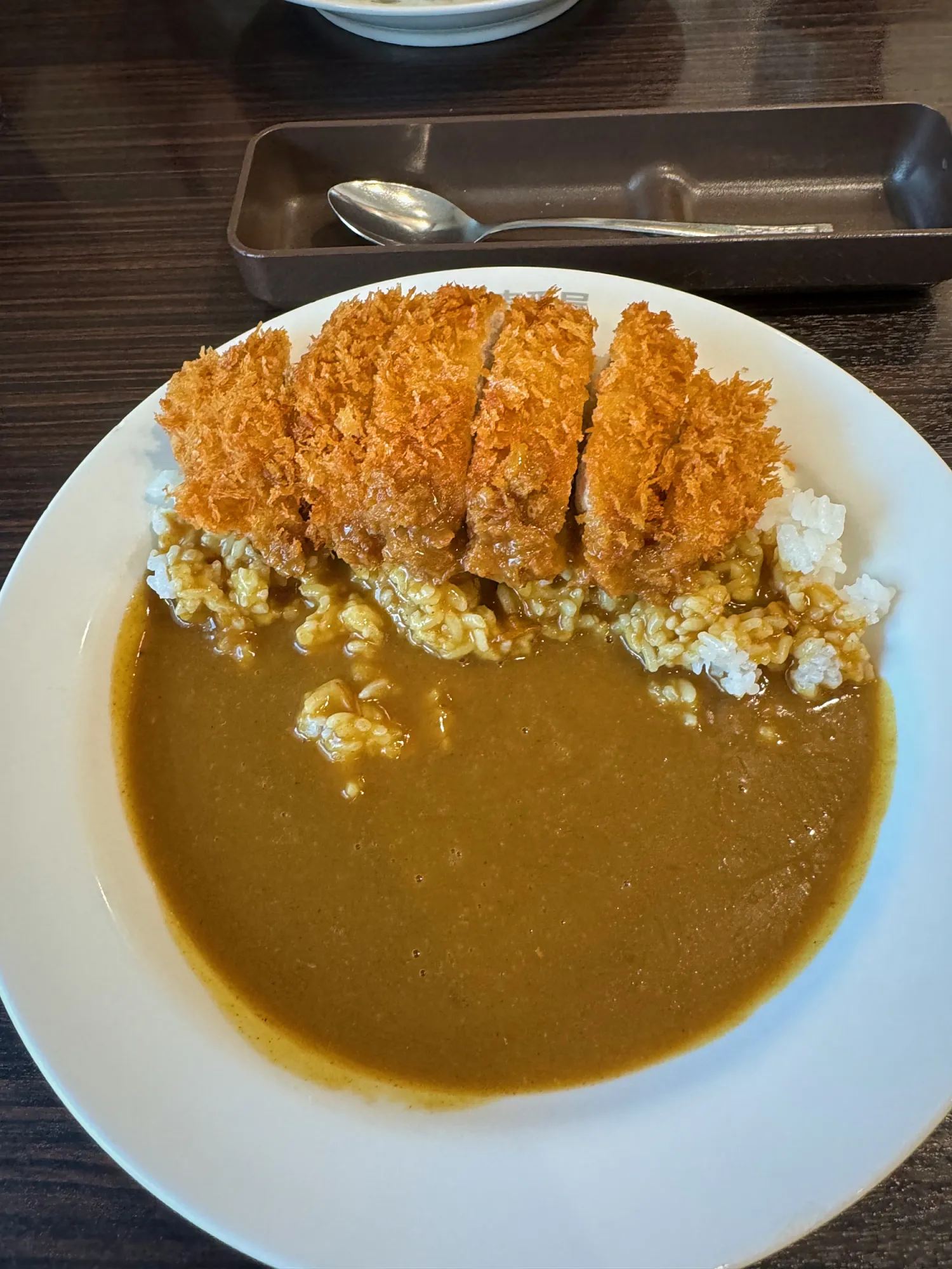 A plate of katsu curry at CoCo Ichibanya in Shinjuku, with the thick sauce pooled on one side and a metal tray of cutlery behind it.