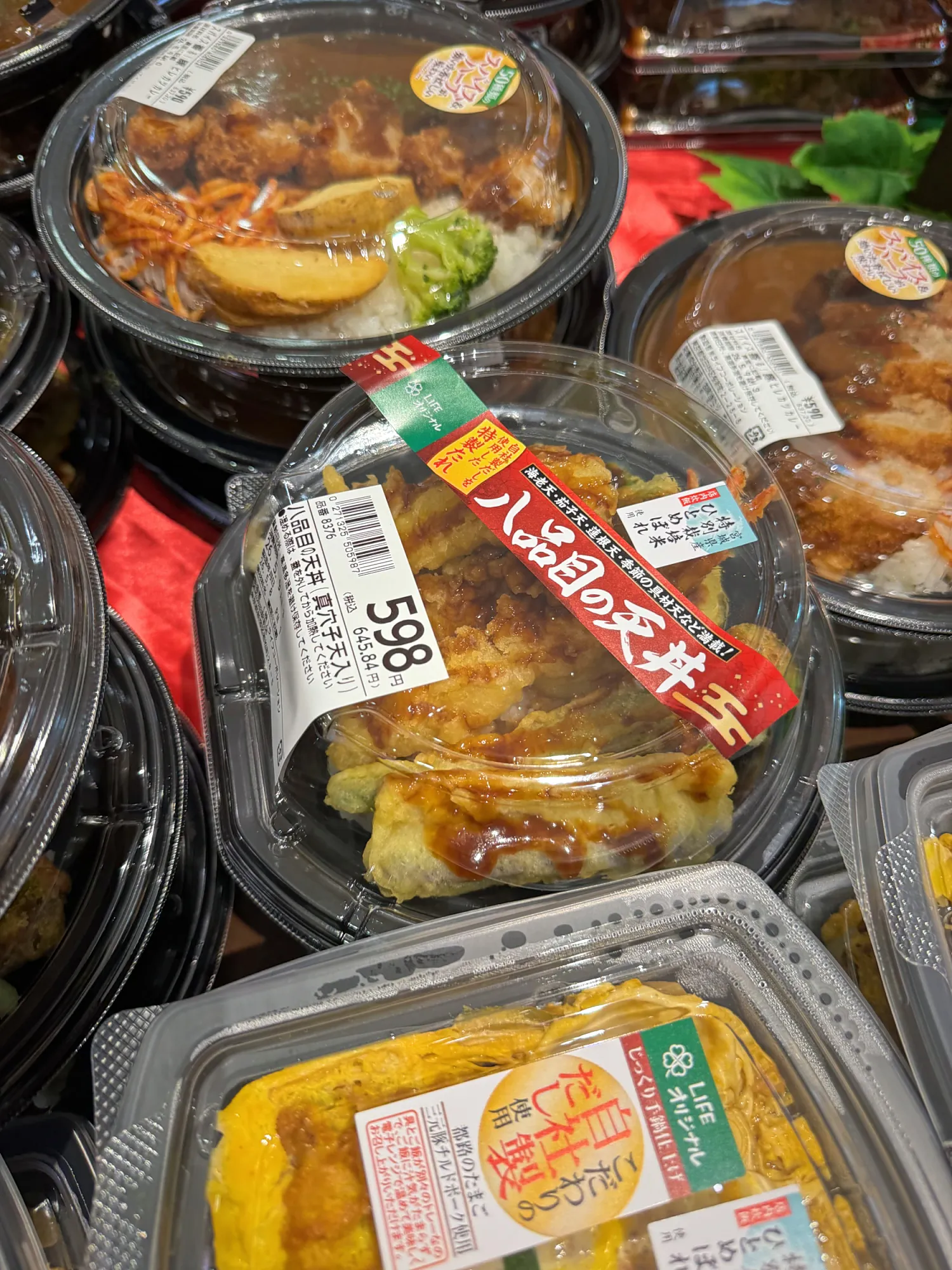 Supermarket bento boxes in Tokyo stacked under 598-yen price stickers, with tempura rice bowls and rolled omelet.