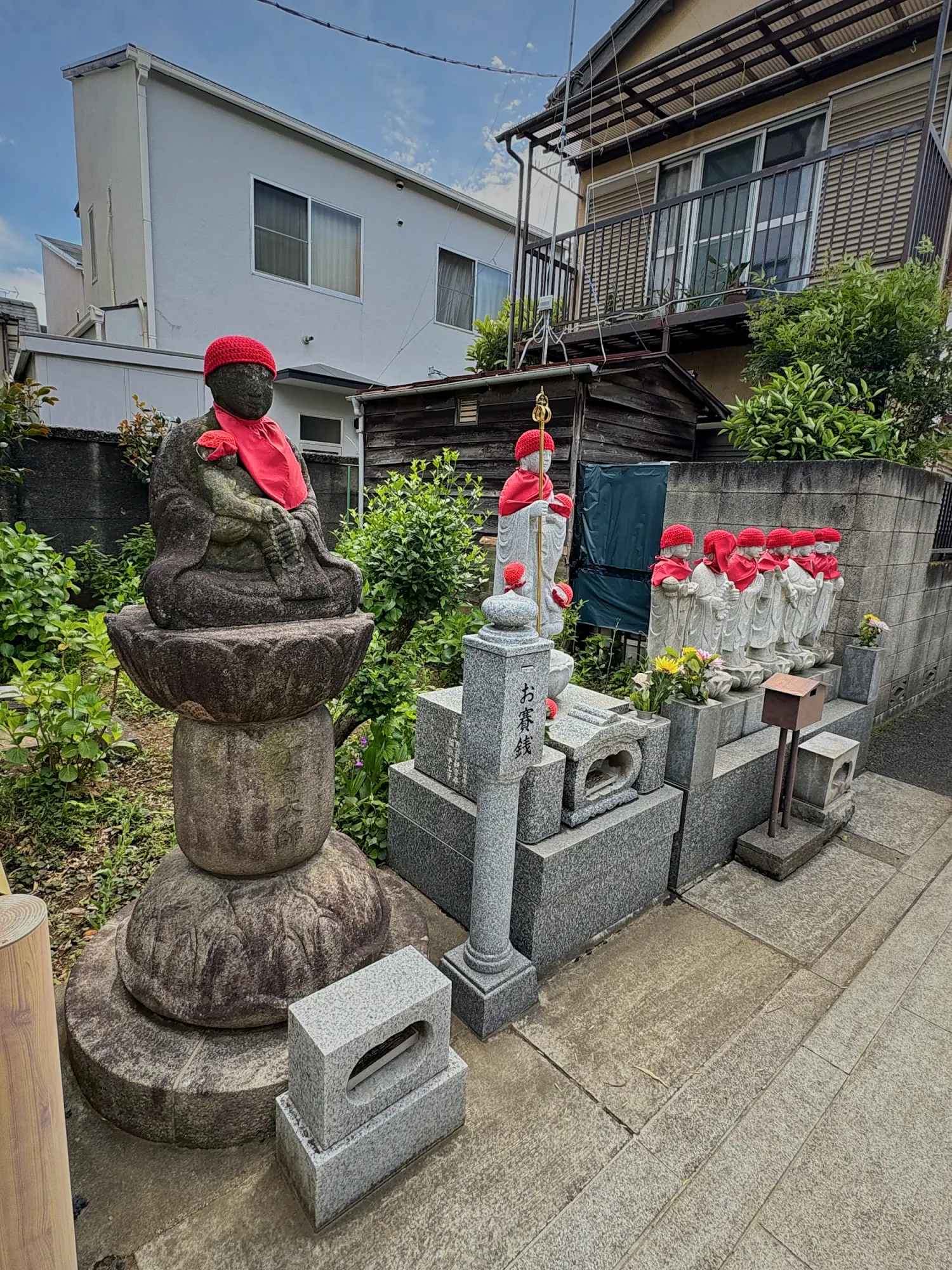 Stone Jizo statues wearing red knitted caps and bibs at a small roadside shrine in Shinjuku City, Tokyo.