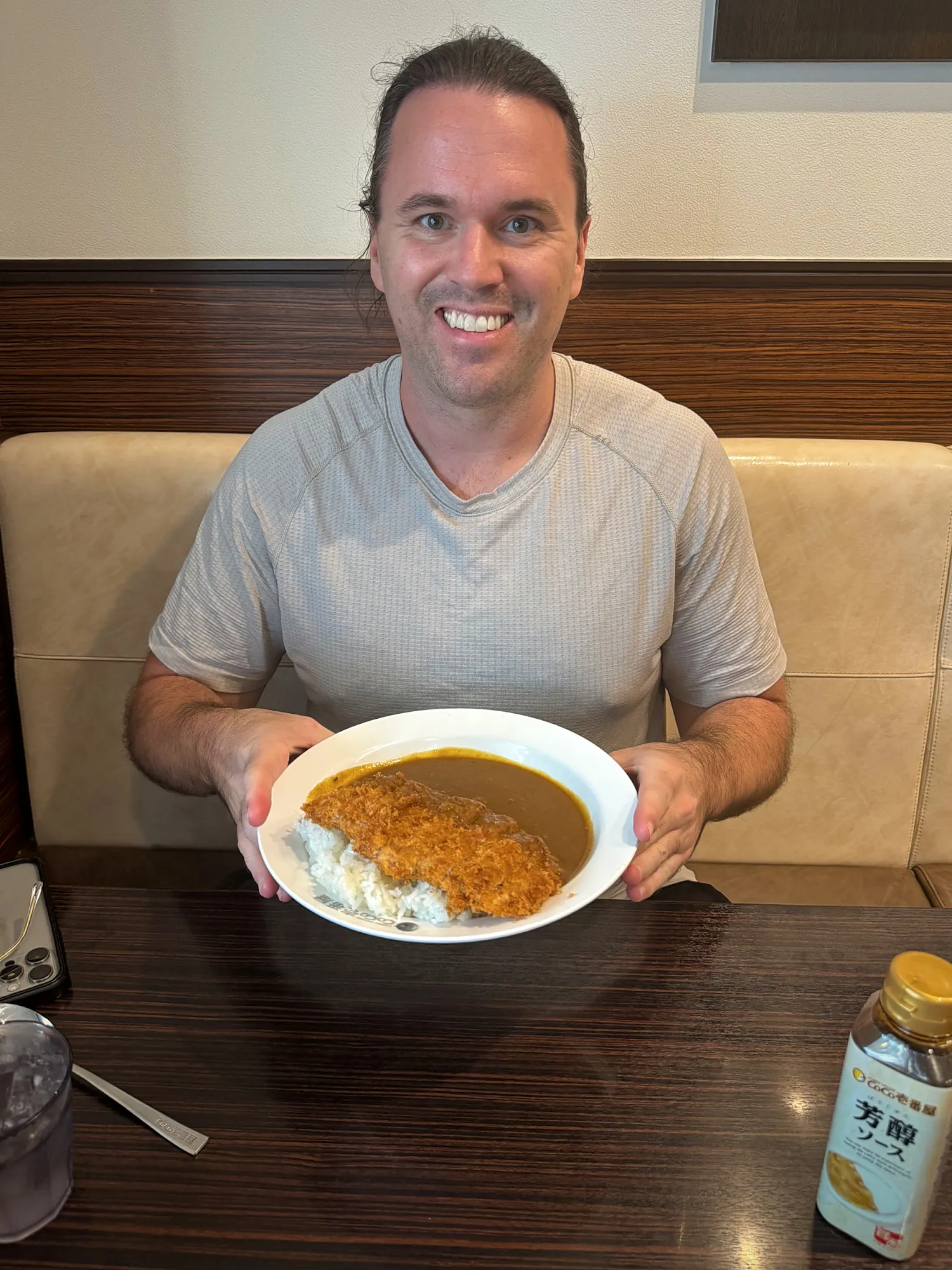 Cream smiling in a CoCo Ichibanya booth in Shinjuku, holding up a plate of katsu curry.