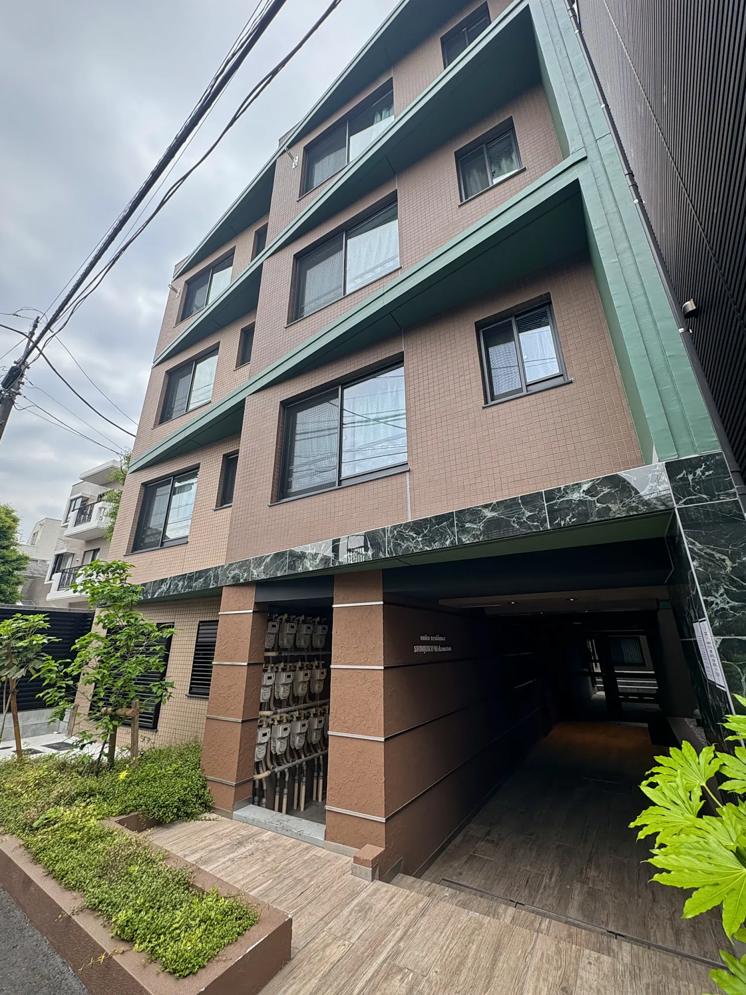 A modern mid-rise apartment building with a wood-paved entrance on a quiet residential street in Tokyo.