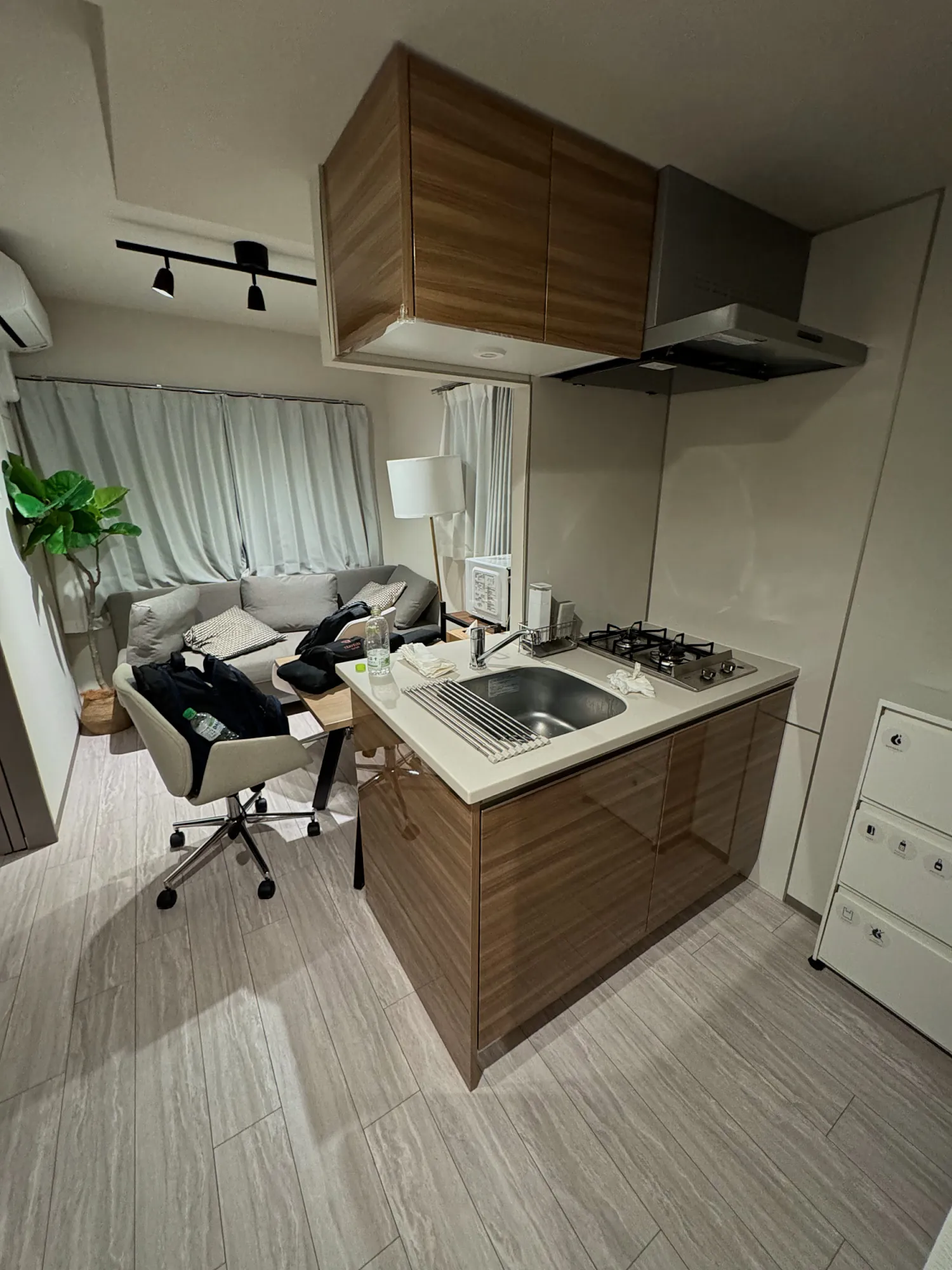 Our apartment at unito residence Shinjuku Wakamatsu in Tokyo, with a wood kitchen counter and two gas burners in front of a gray sofa and curtained windows.