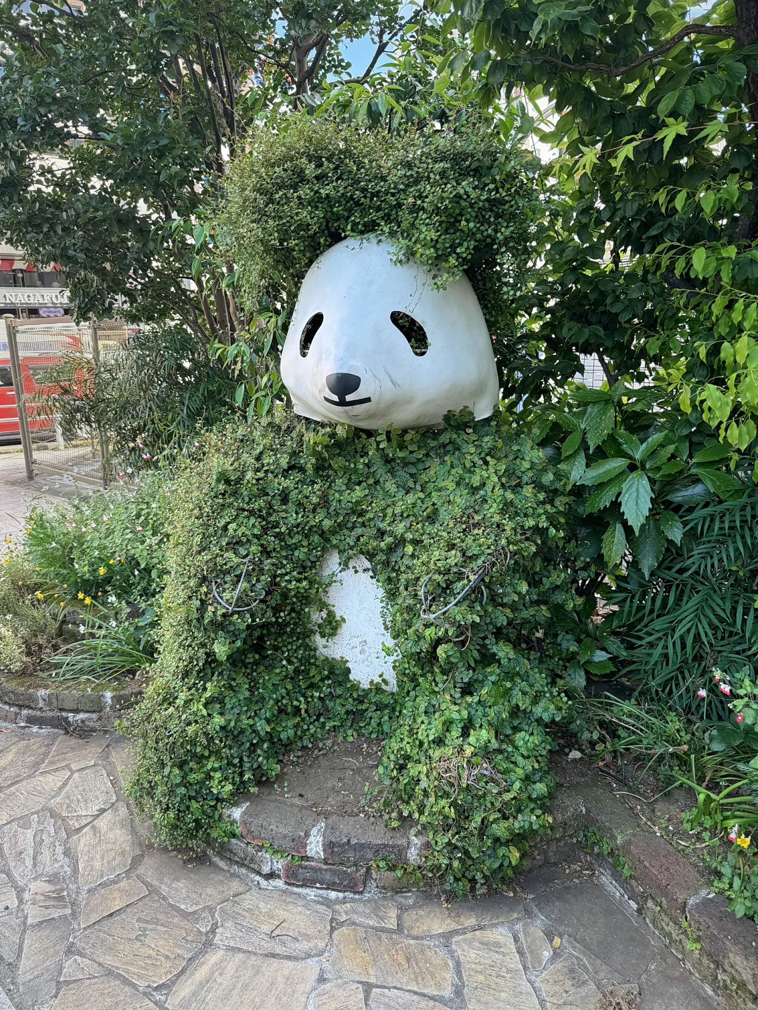 A panda topiary covered in green leaves in Ueno, Tokyo, with a white panda face peeking out of the plants.