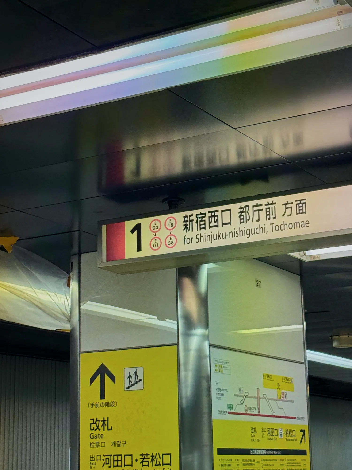 A platform 1 sign on the Oedo Line reading for Shinjuku-nishiguchi and Tochomae, with a yellow sign pointing up to the gates.