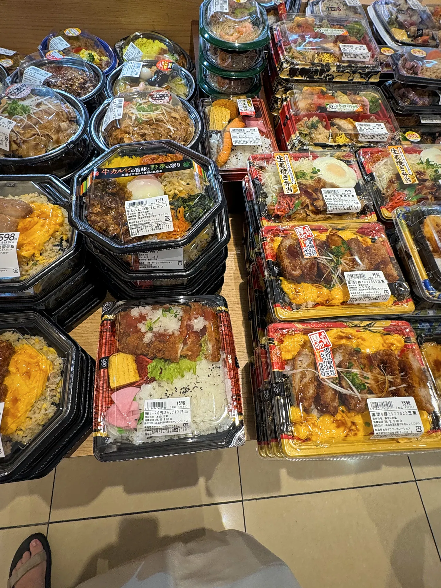 Rows of packaged bento boxes with fried chicken, rice, and noodles at a Tokyo supermarket