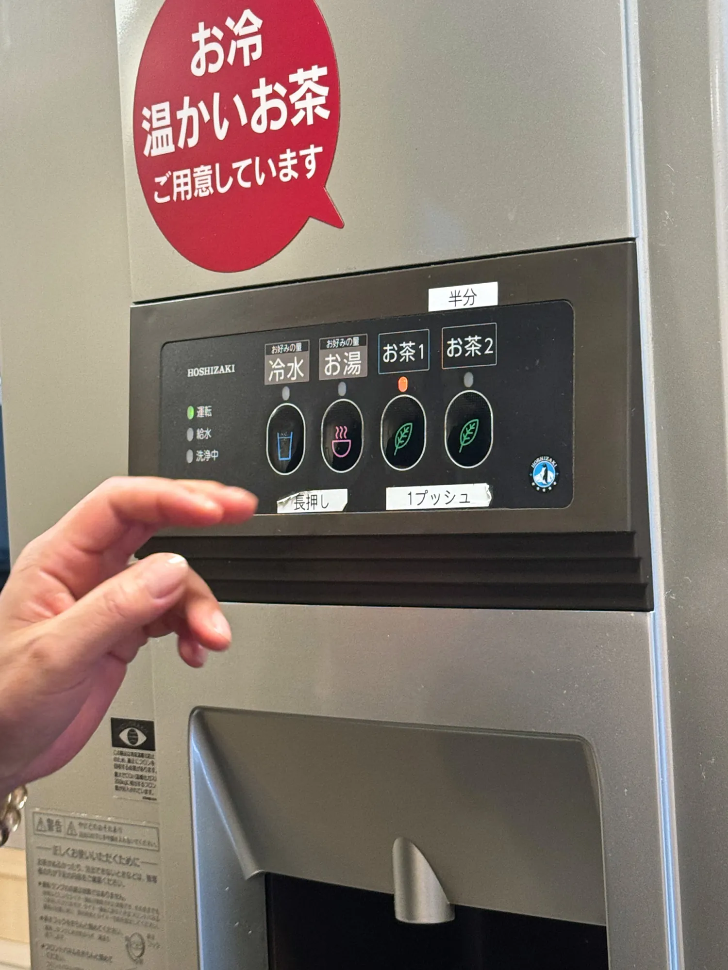A hand by the buttons of a free hot and cold tea and water dispenser in Tokyo.