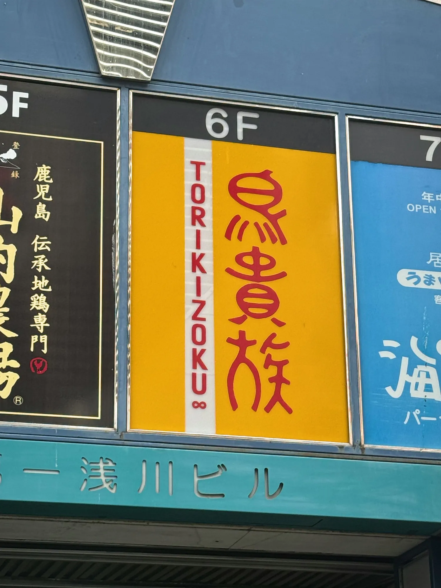 Vertical restaurant signs stacked on a Tokyo building, with the yellow Torikizoku sign marked 6F for the sixth floor.