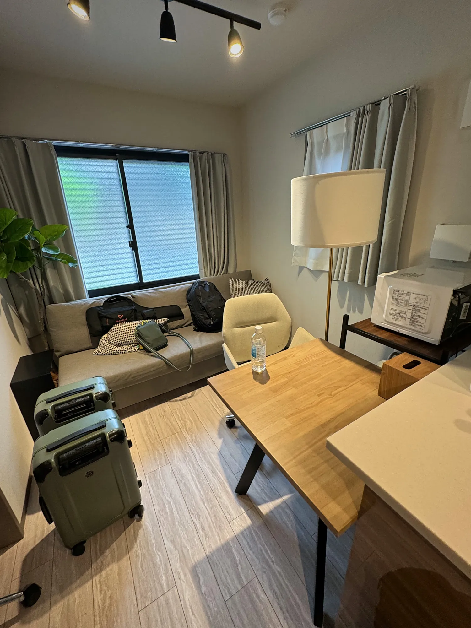 Two green suitcases and backpacks just inside a small, bright apartment living room in Shinjuku, Tokyo.