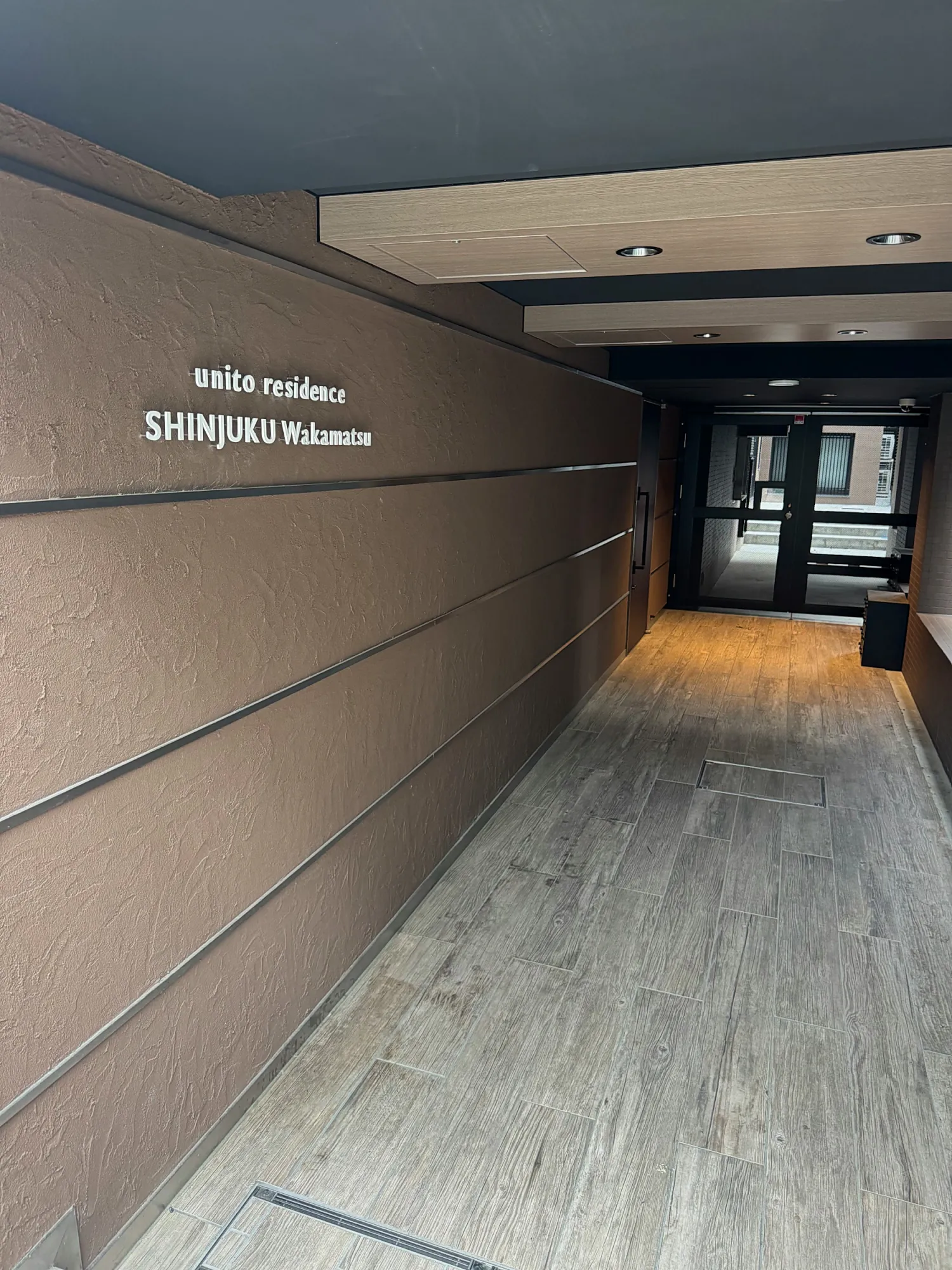 The tiled entrance hallway of unito residence Shinjuku Wakamatsu, with the building's name on the wall.