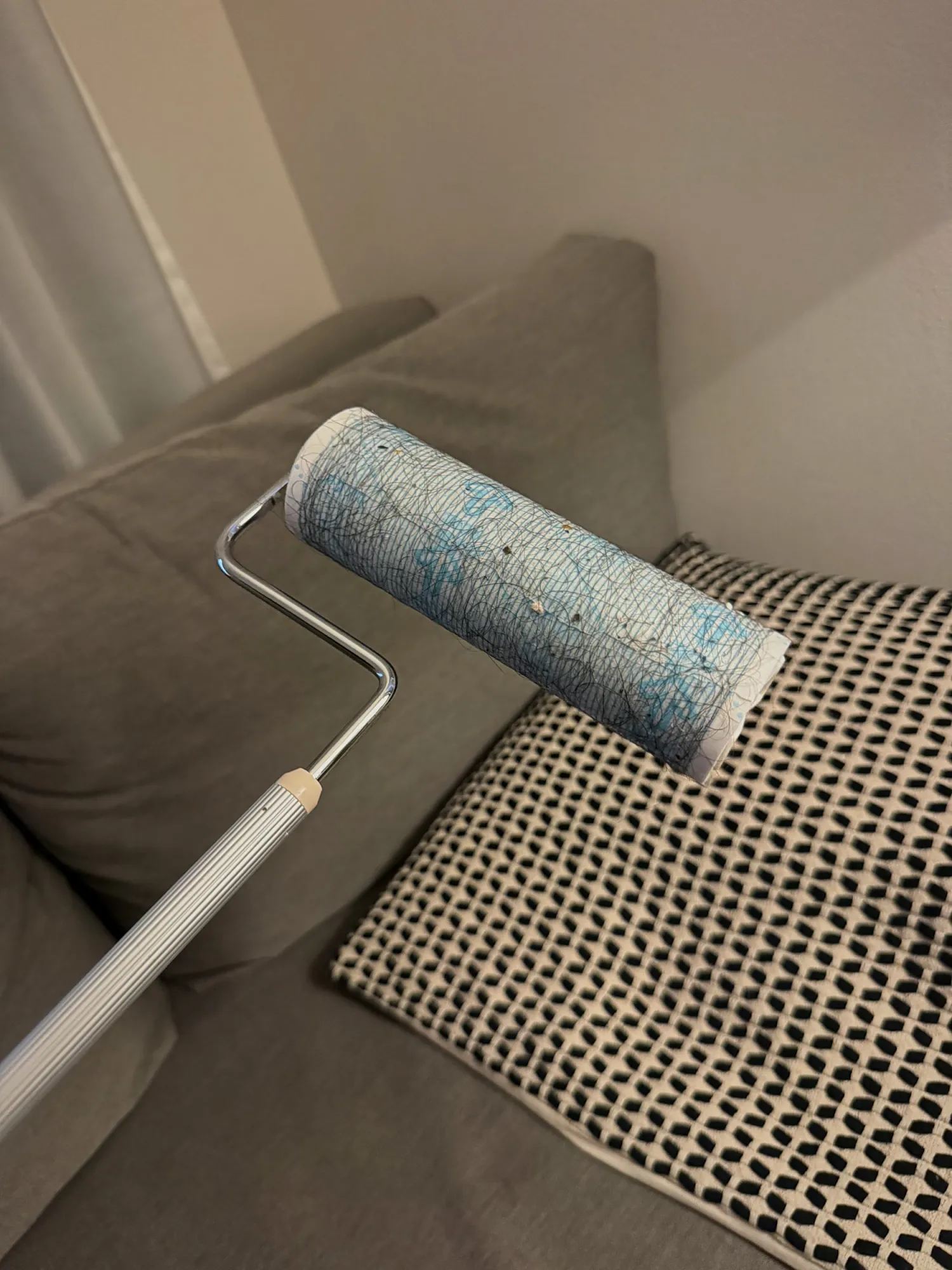 A long-handled sticky floor roller resting on a gray sofa in our Tokyo apartment.