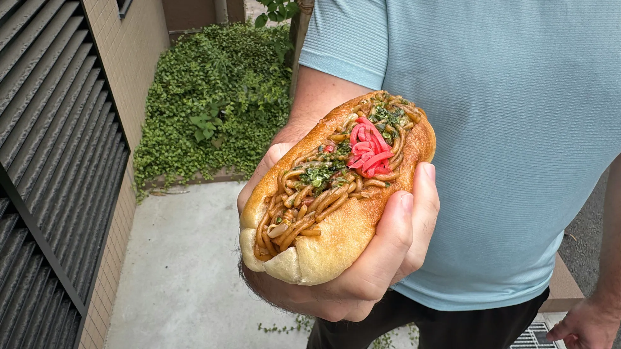 A yakisoba pan, fried noodles with pickled ginger in a soft bun, held on a street in Shinjuku