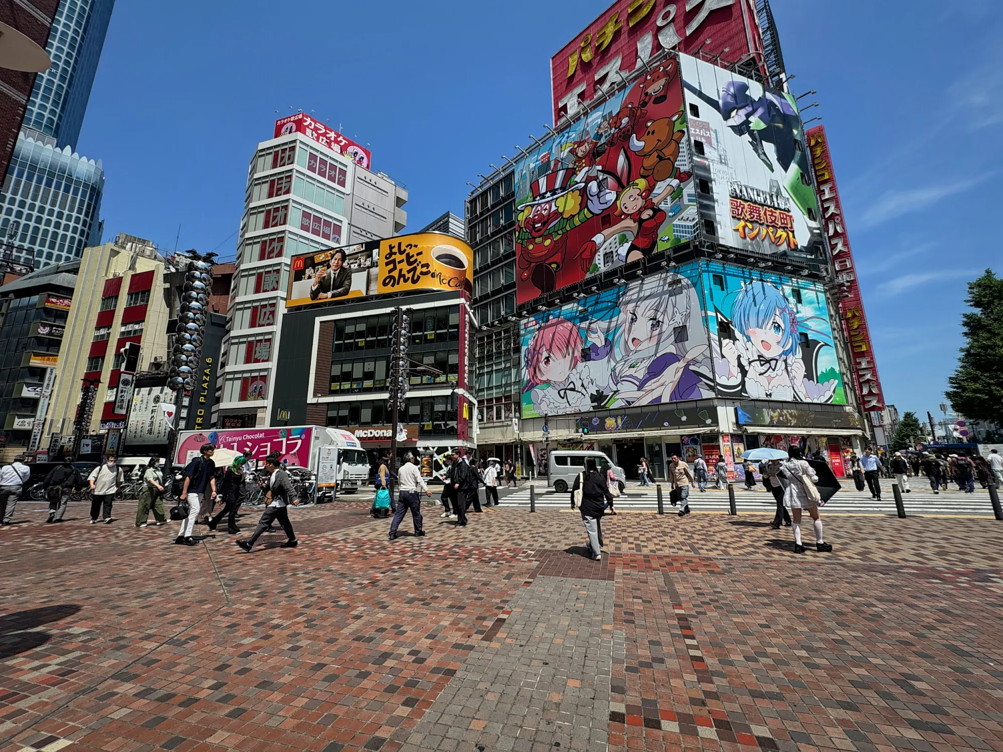 People crossing a paved square in Akihabara, Tokyo, under buildings covered in giant colorful anime billboards.