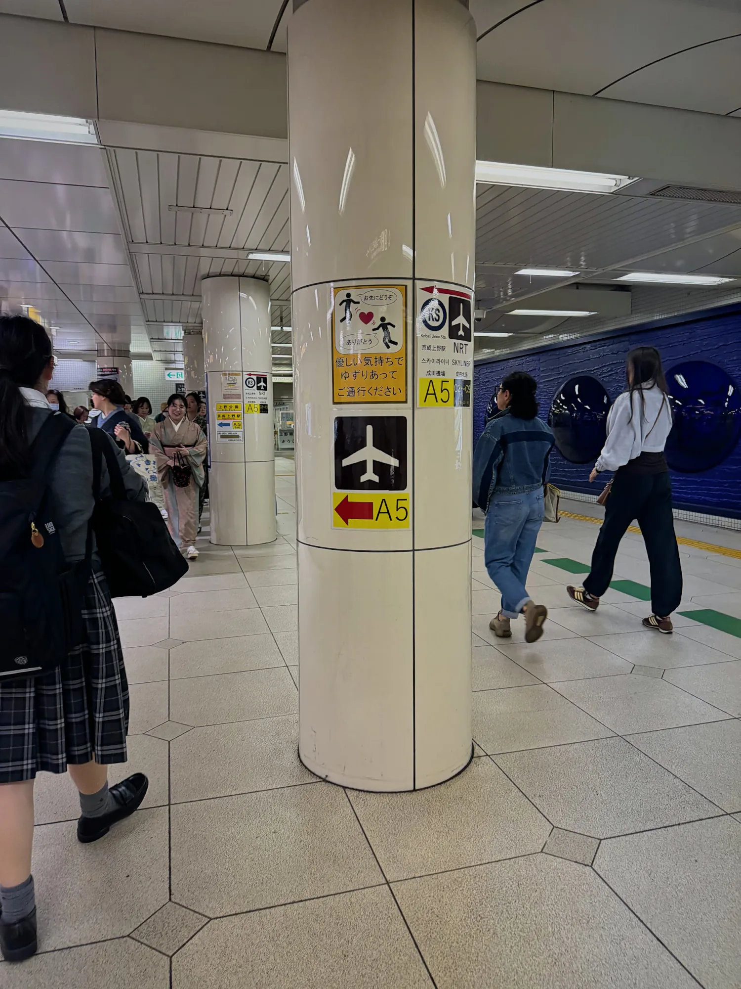 A pillar in Ueno-okachimachi Station with a yellow sign for exit A5 and an airplane symbol for the Keisei Skyliner to Narita Airport.
