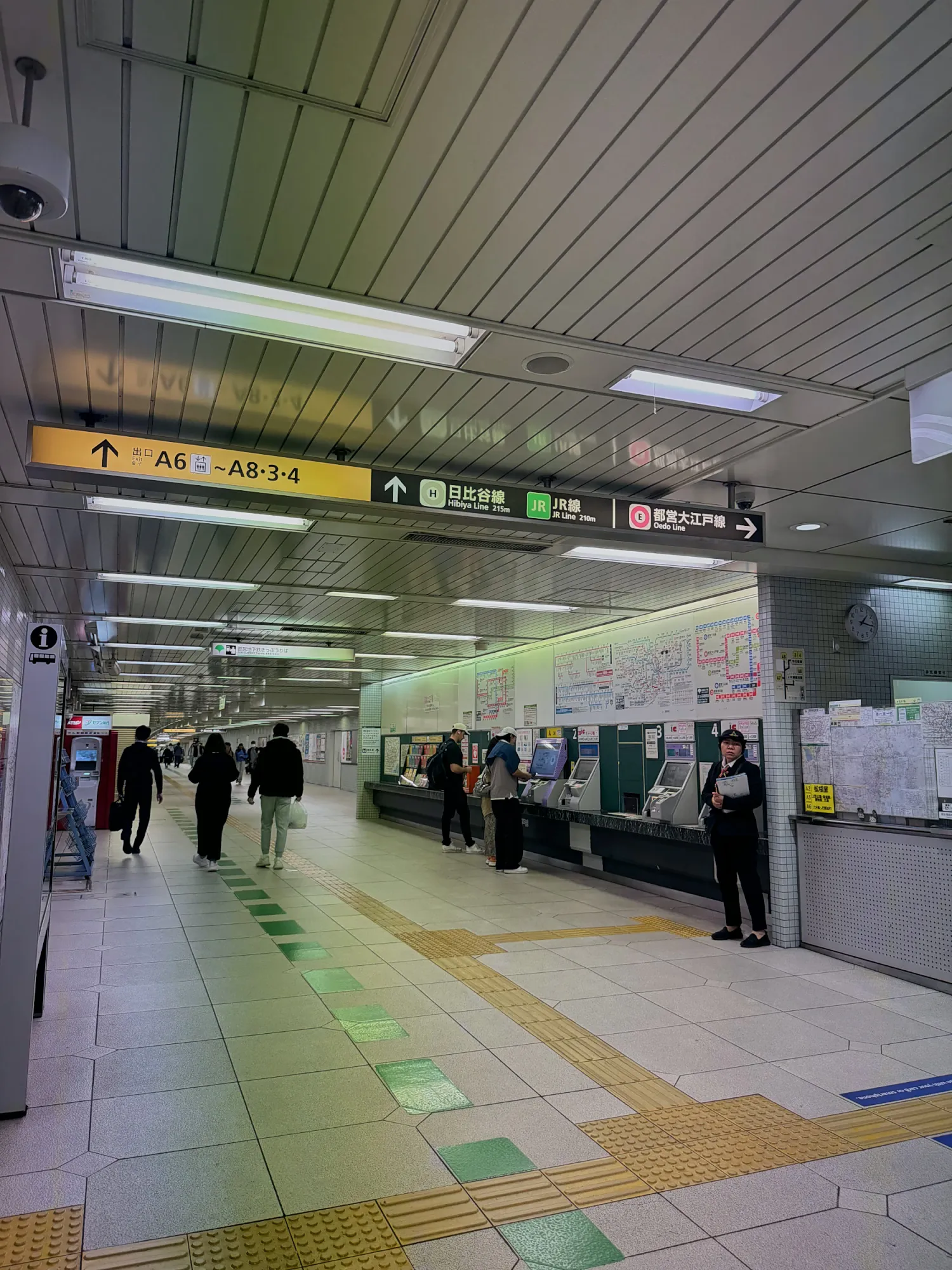 A Tokyo subway concourse with a row of ticket machines on the right, green floor arrows, and overhead signs pointing to exits A6 to A8 and other lines.