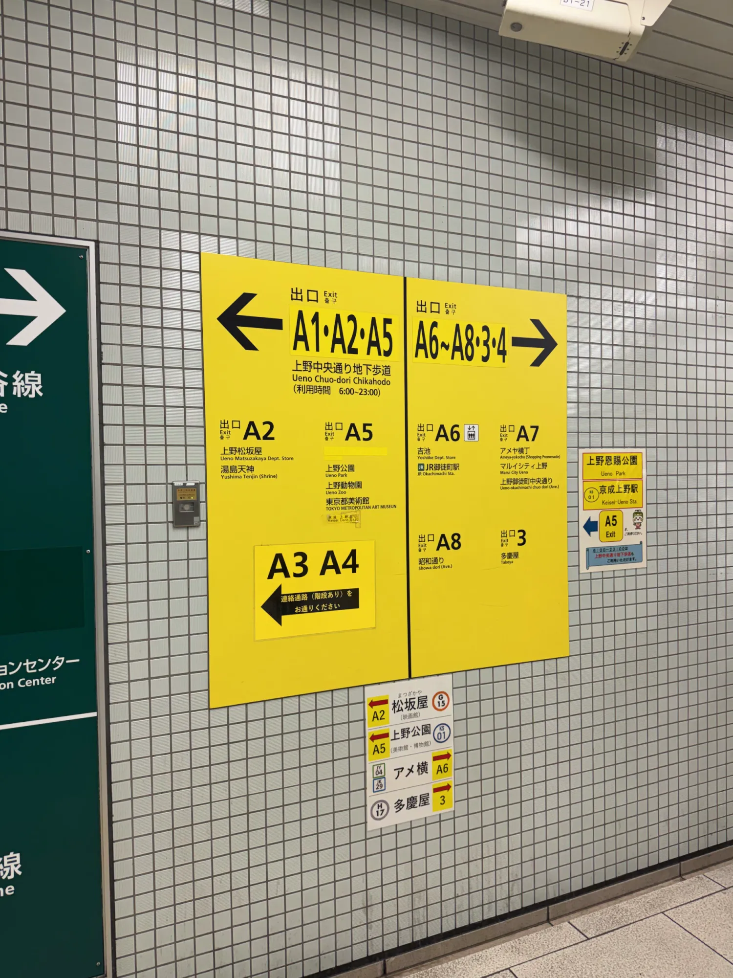 Yellow subway exit signs in a Tokyo station with arrows pointing to exits A1, A2, and A5 one way and A6 to A8 the other.