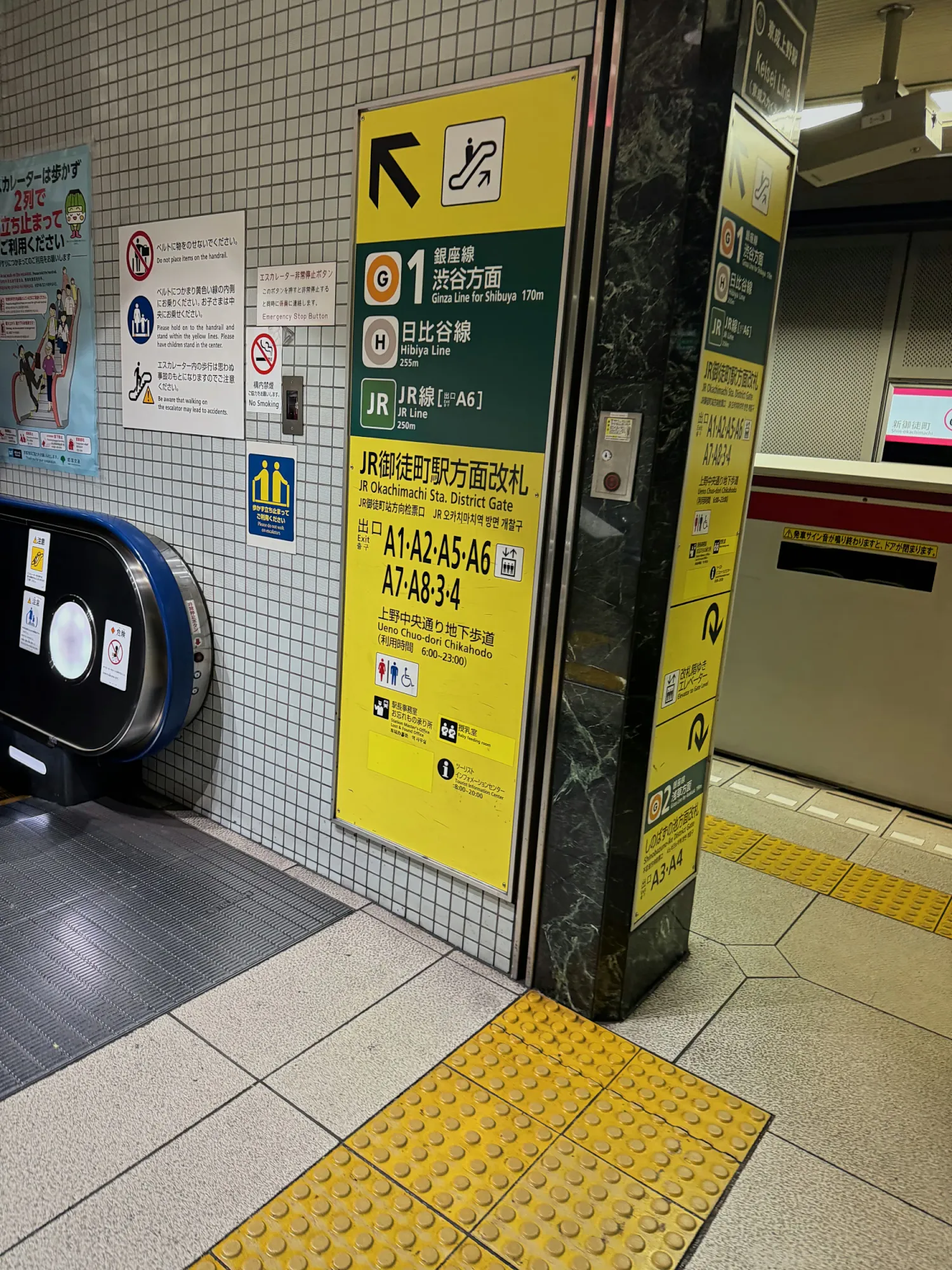 Yellow exit signs listing exits A1 to A8 on a pillar beside an escalator in a Tokyo subway station.