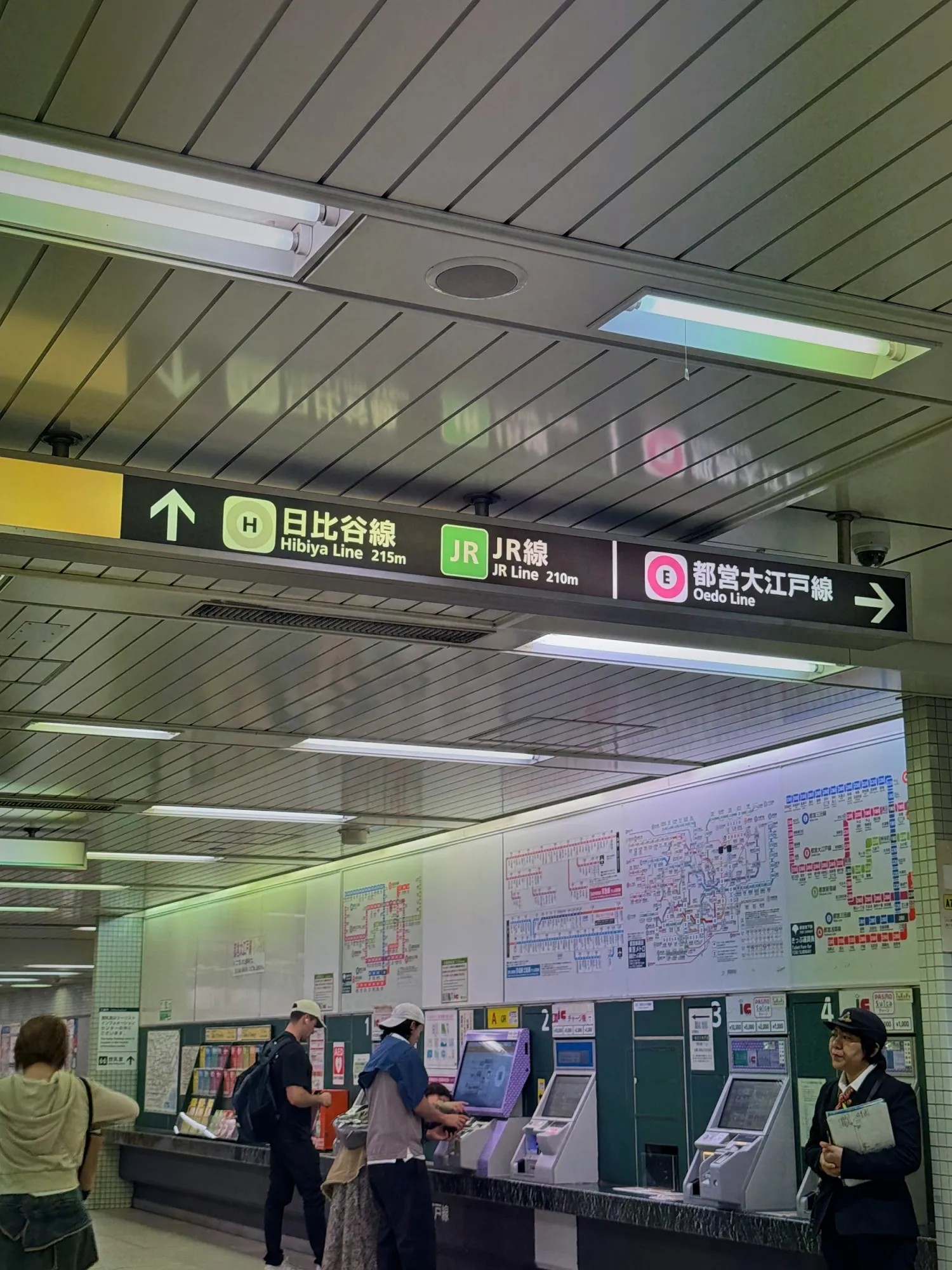 Overhead signs in a Tokyo subway station showing line names and exits in both Japanese and English.