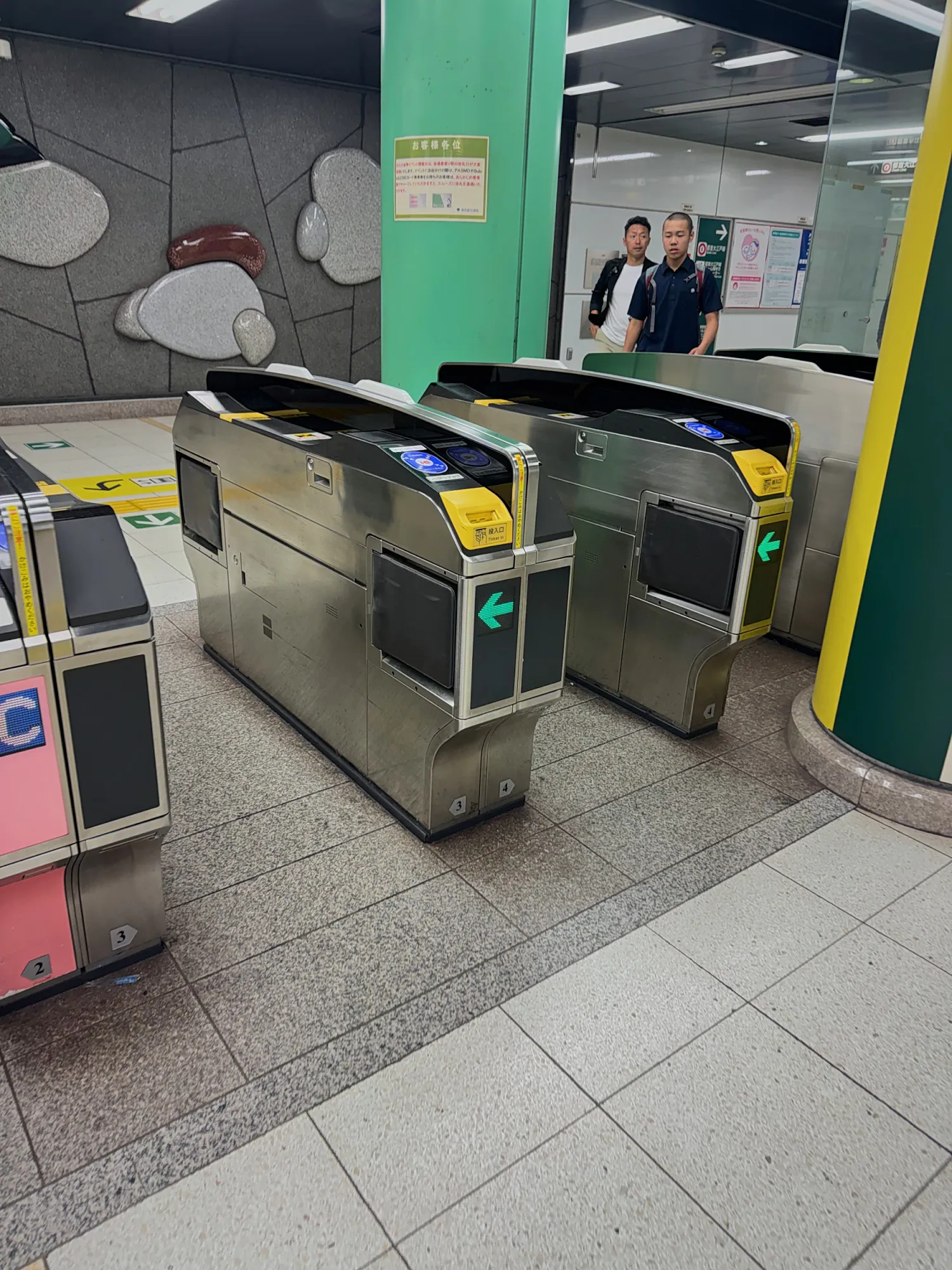 Empty ticket gates at a Tokyo subway station, with green pillars and a pink ticket machine on the left.